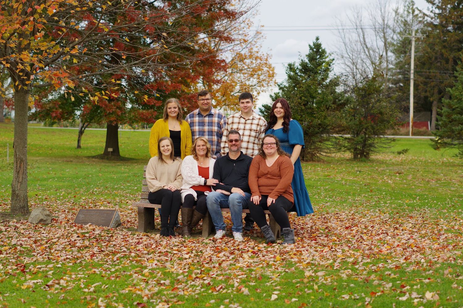 Group outdoor photo session with autumn trees and scattered leaves on the ground.