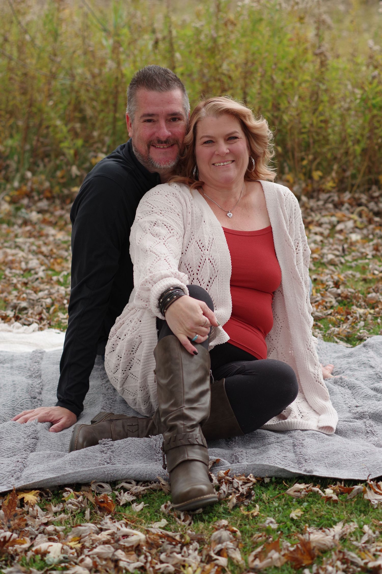 A cozy autumn portrait of a couple sitting on a blanket surrounded by fallen leaves.