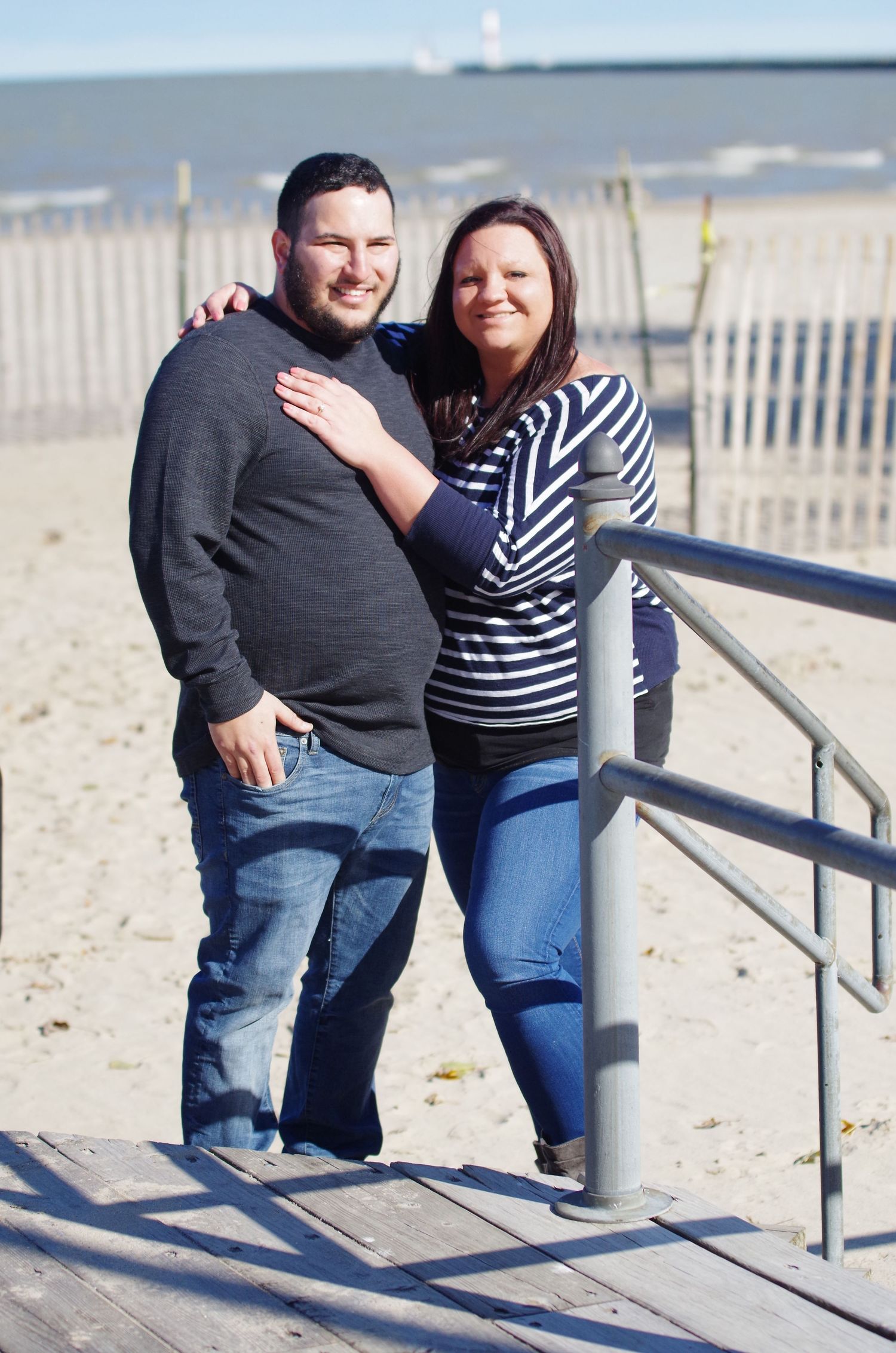 Couple embracing on beach boardwalk with ocean view.