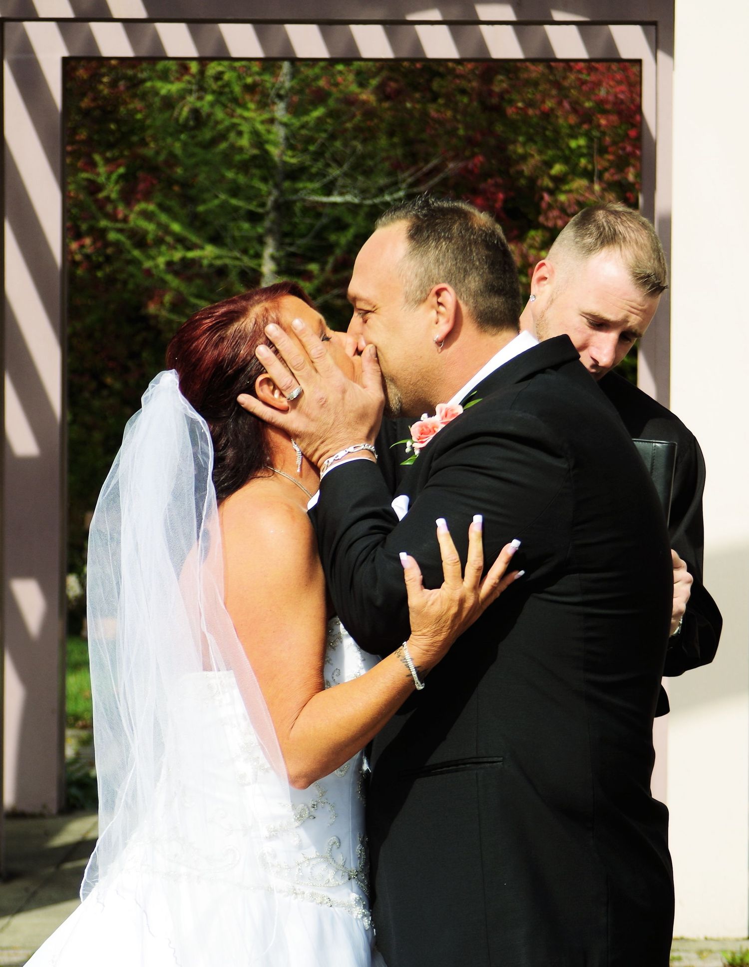 Wedding party sharing first kisses in sequence under striped architectural details.
