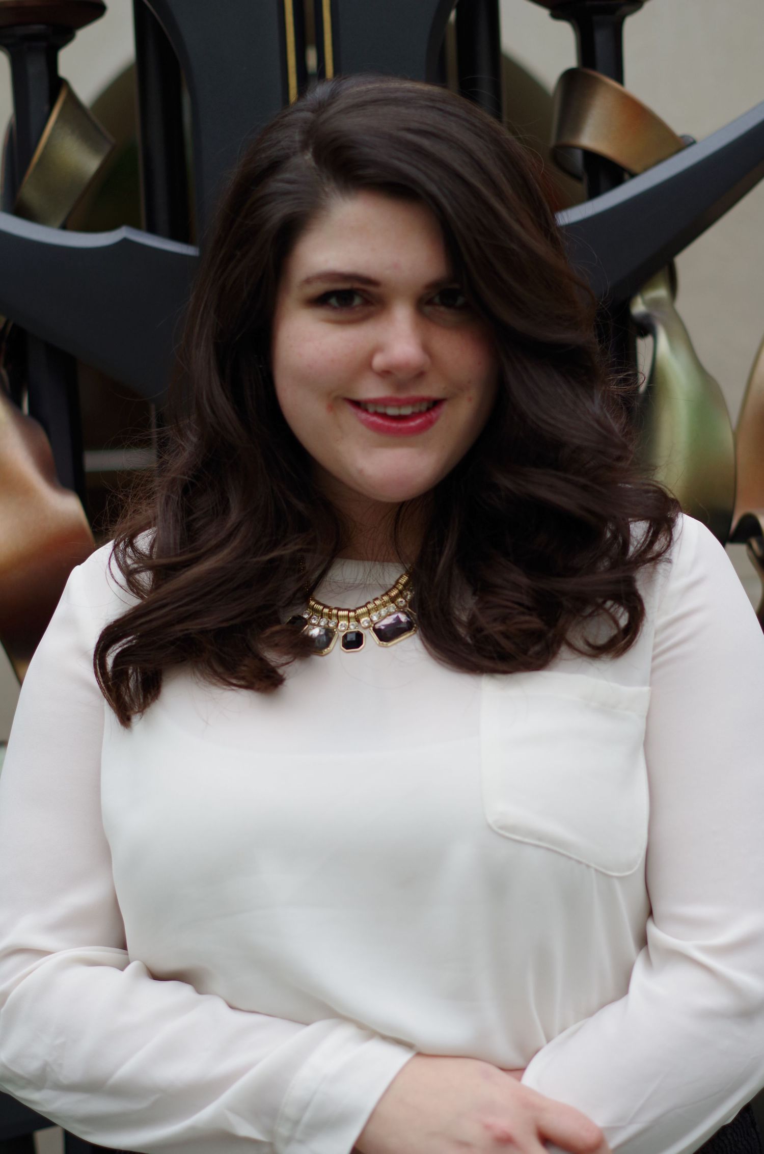 A person in a white blouse with statement necklace poses for a portrait.