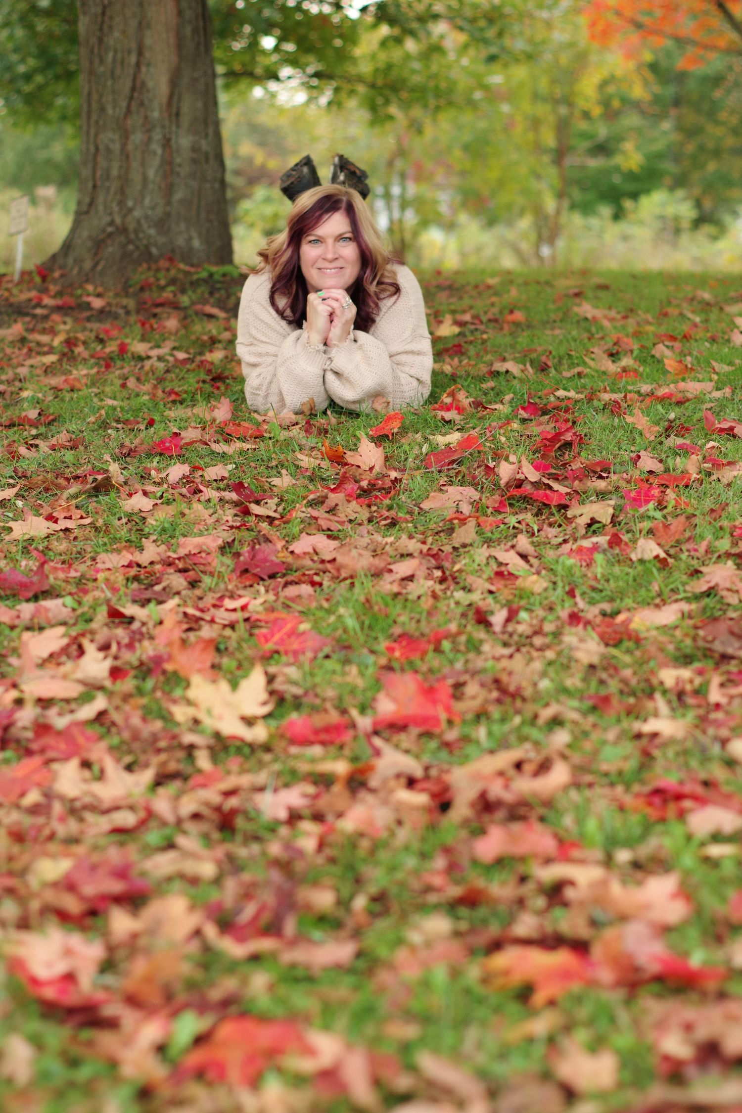 Person lying on autumn ground covered in red maple leaves wearing cream sweater.