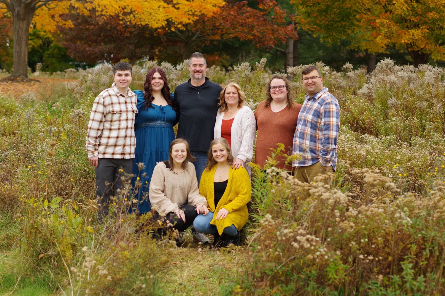 Outdoor family portrait with golden autumn colors and wildflowers in background.