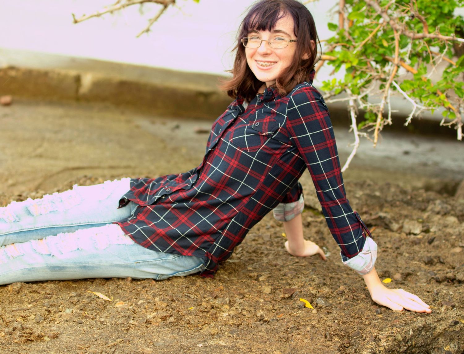 Playful outdoor pose on ground wearing plaid dress.