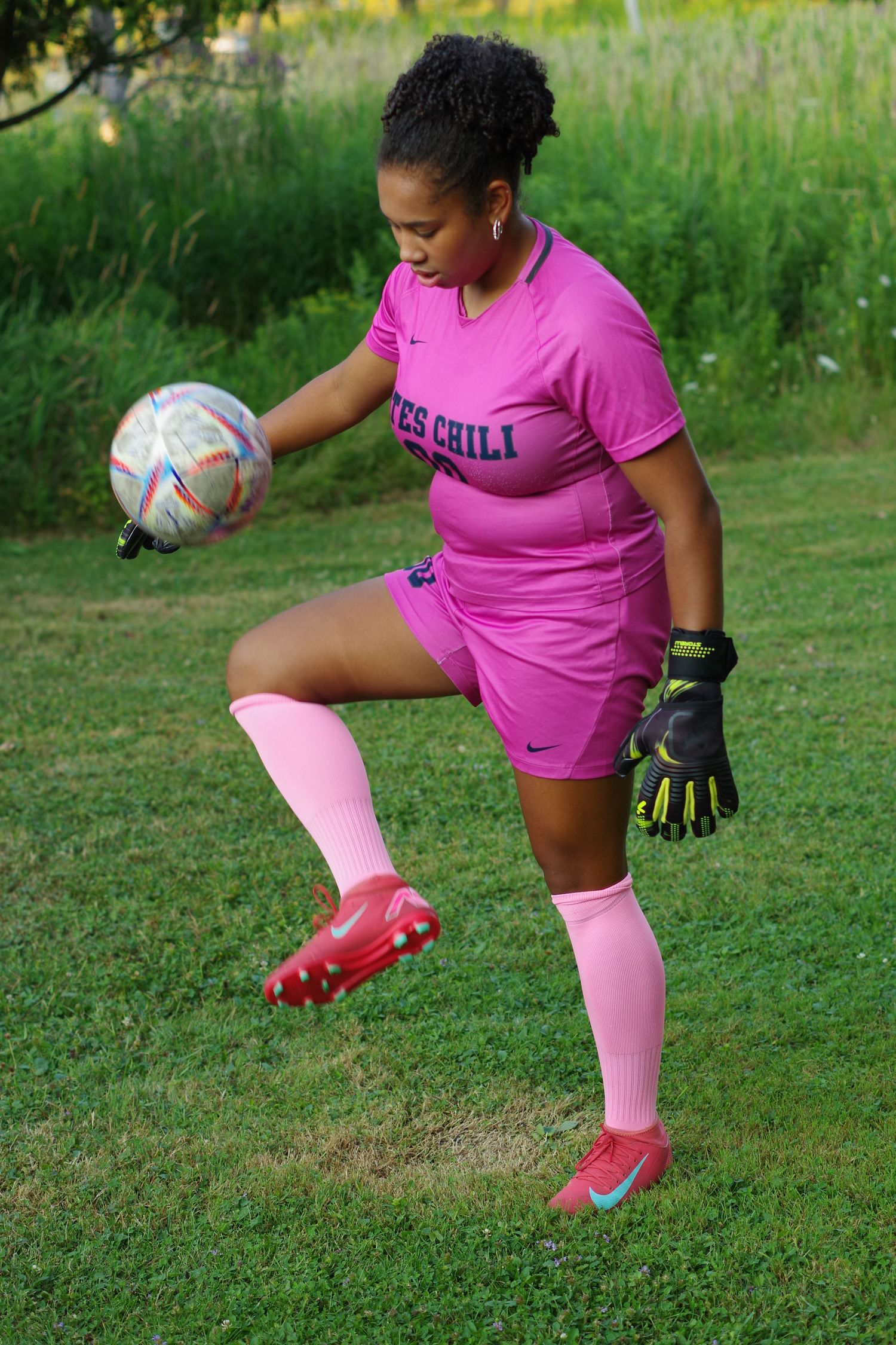 An athlete in pink soccer uniform practices ball control on a grassy field.