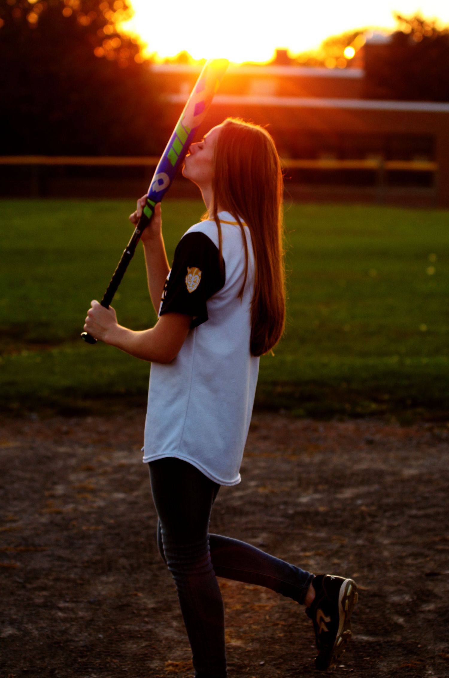 Baseball player silhouetted at sunset holding a bat and showing batting stance posture.