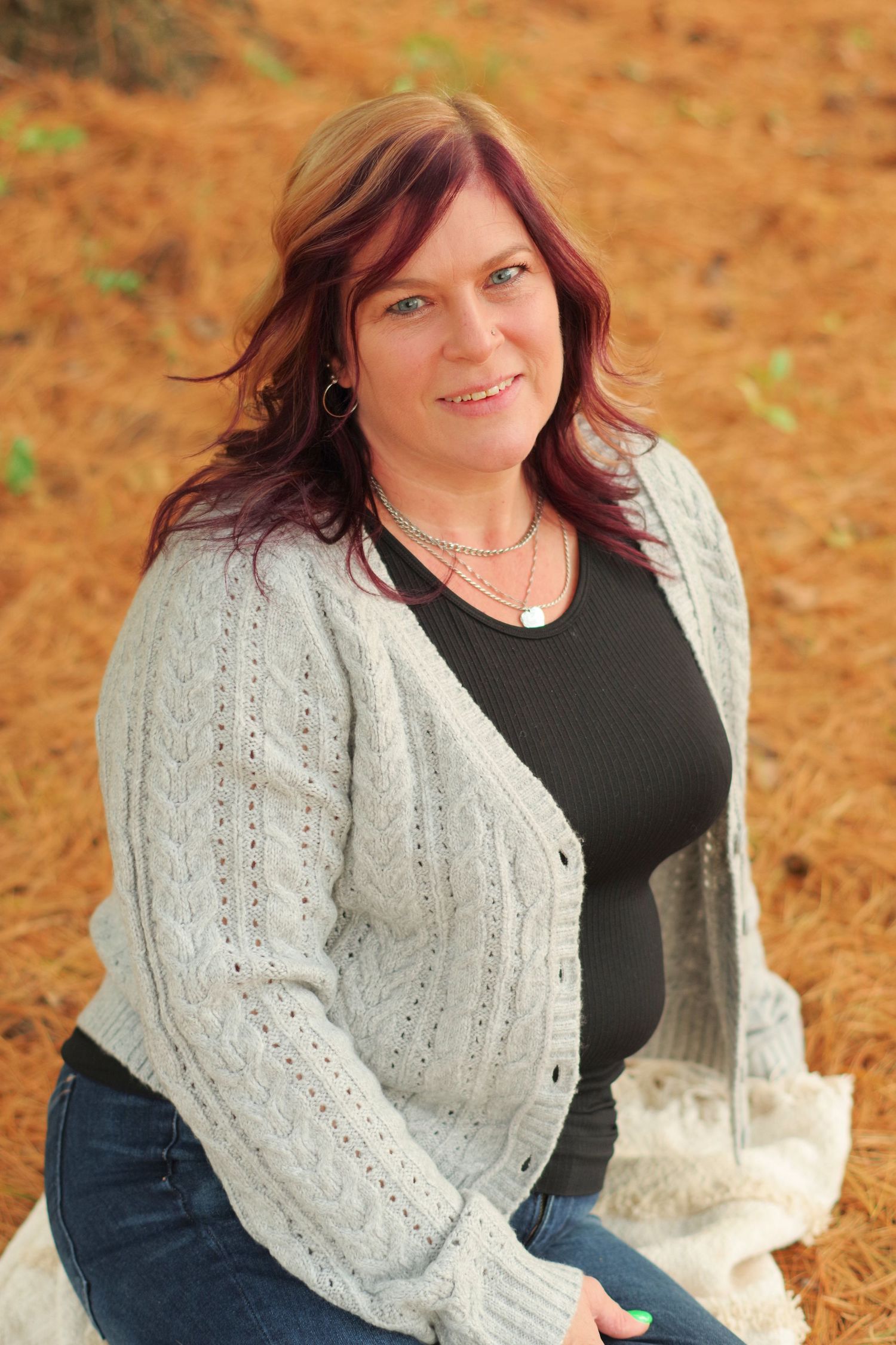 Person in casual outfit poses while wearing a cream colored cable knit cardigan outdoors.
