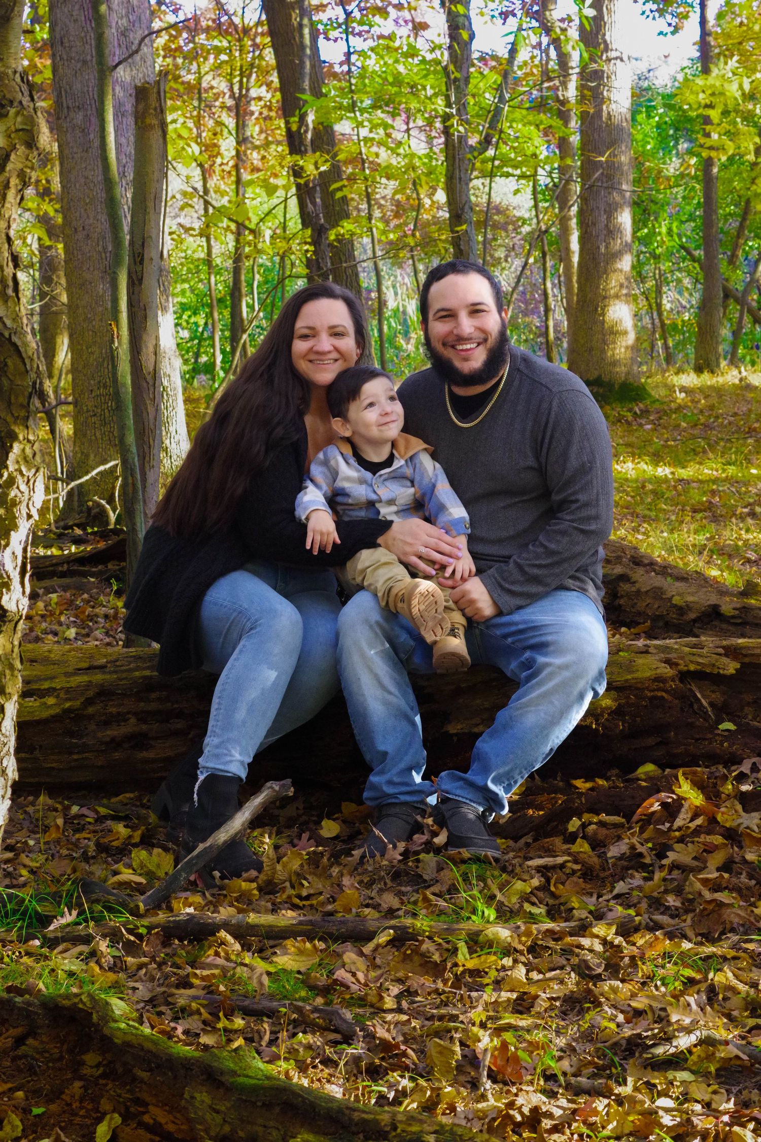 Family sits together on mossy log in wooded setting during autumn season.