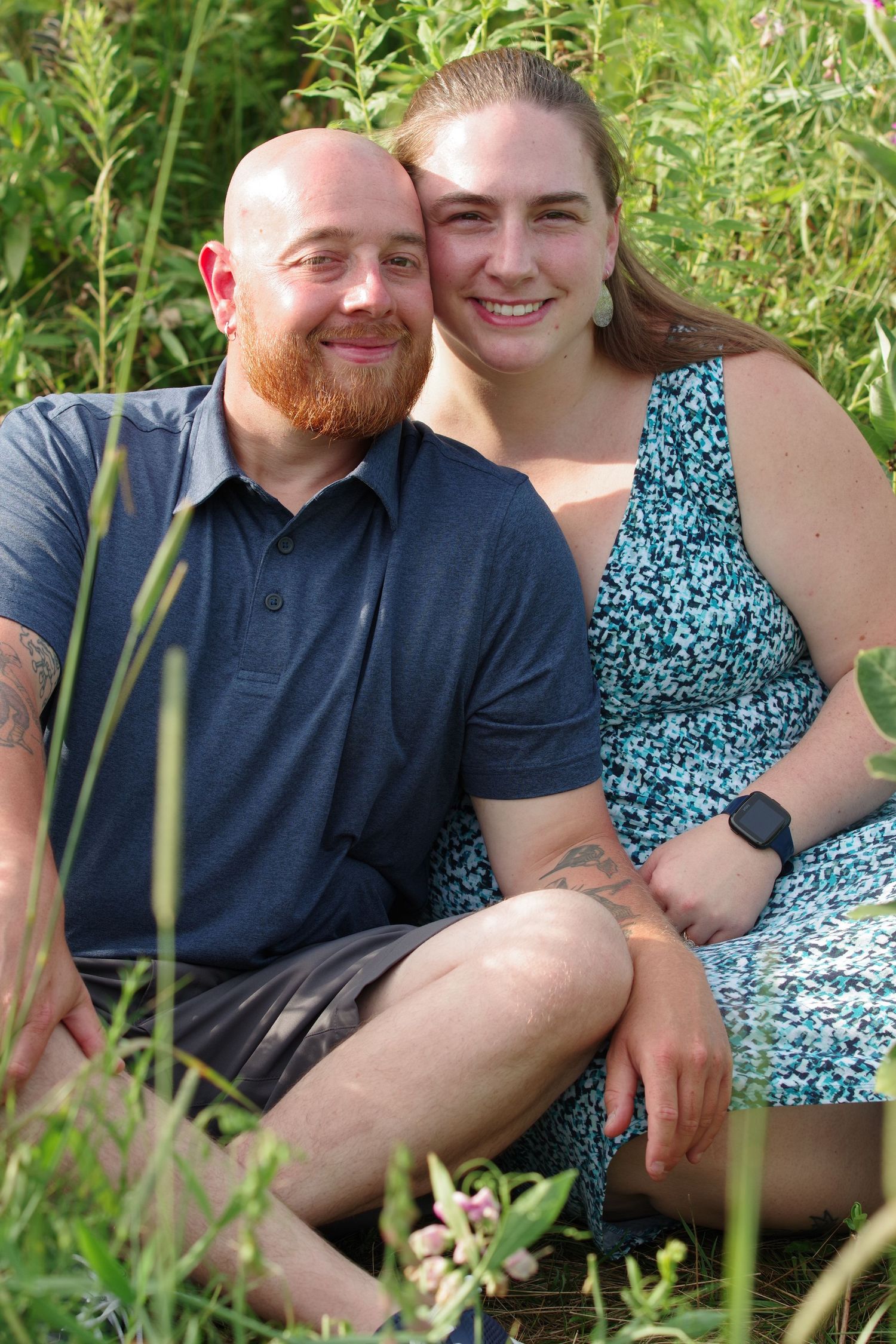 Casual outdoor portrait with couple sitting in green summer foliage.