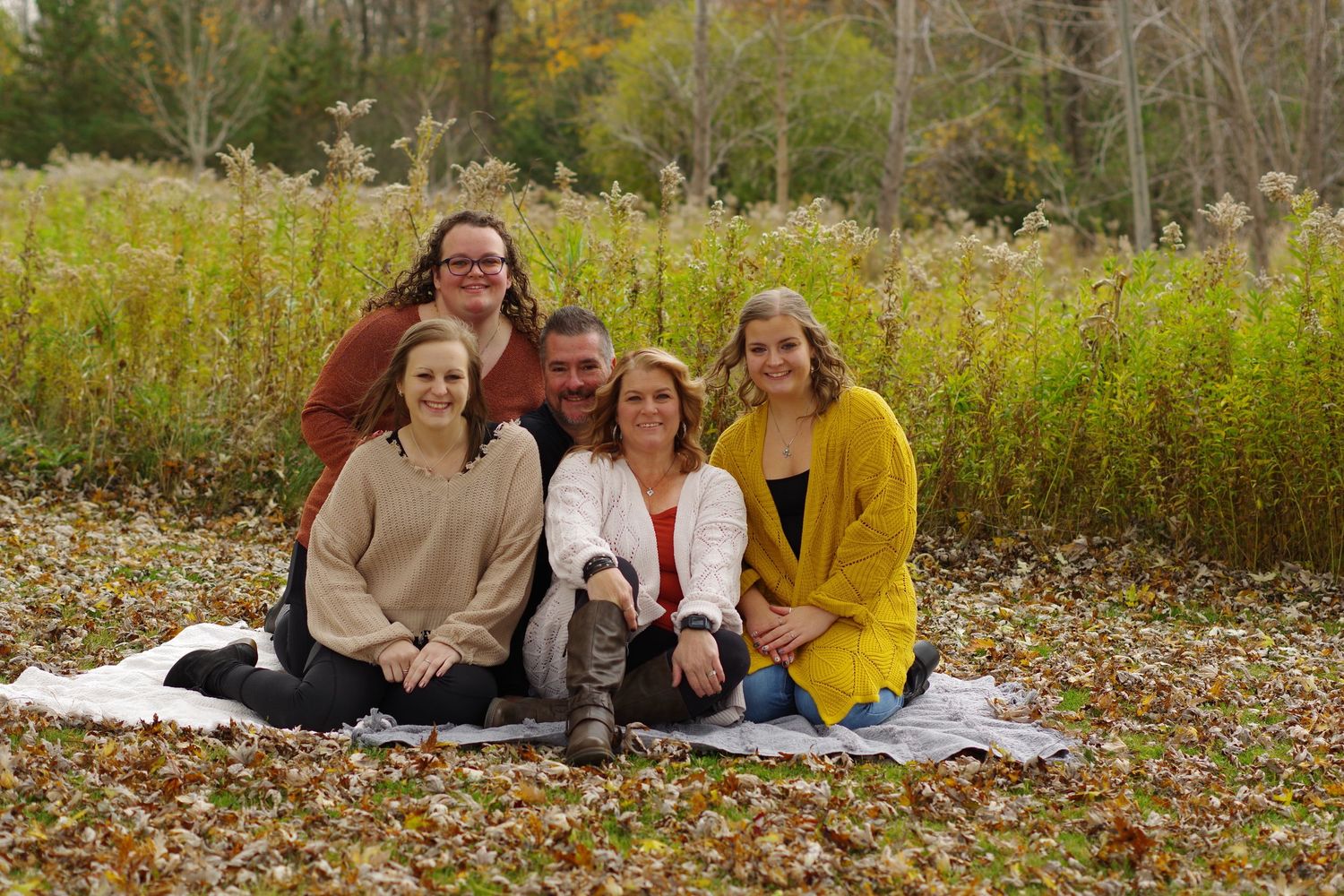 Group photo on white blanket surrounded by tall autumn grass and fall colors.