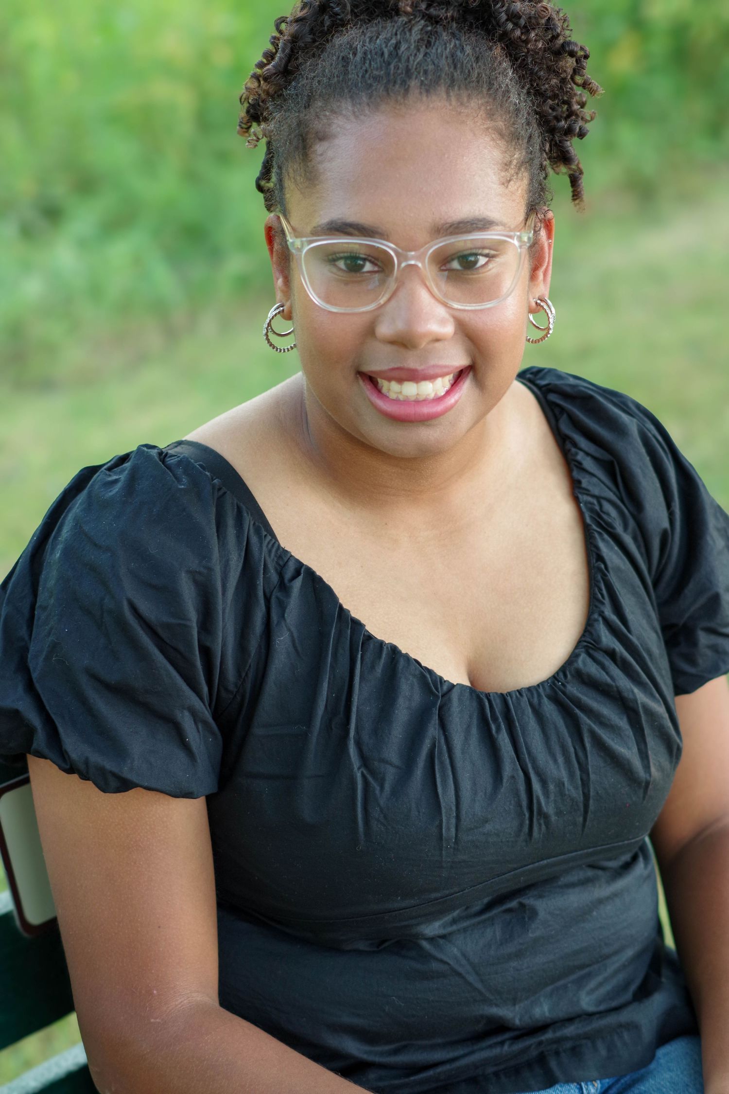 Person in a black top and glasses smiling at the camera while posing on a wooden deck.