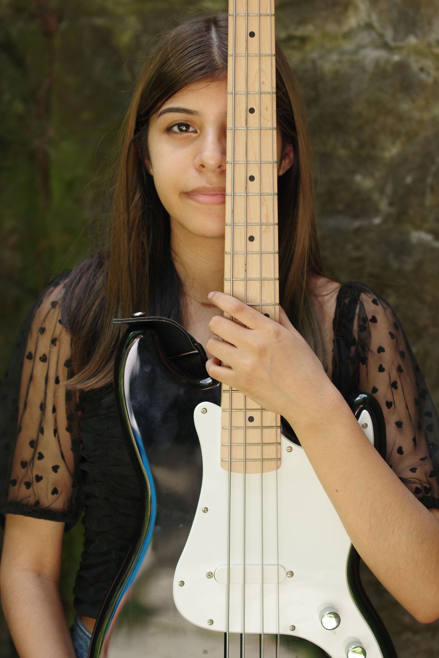 Person posing with white electric bass guitar against dark background.