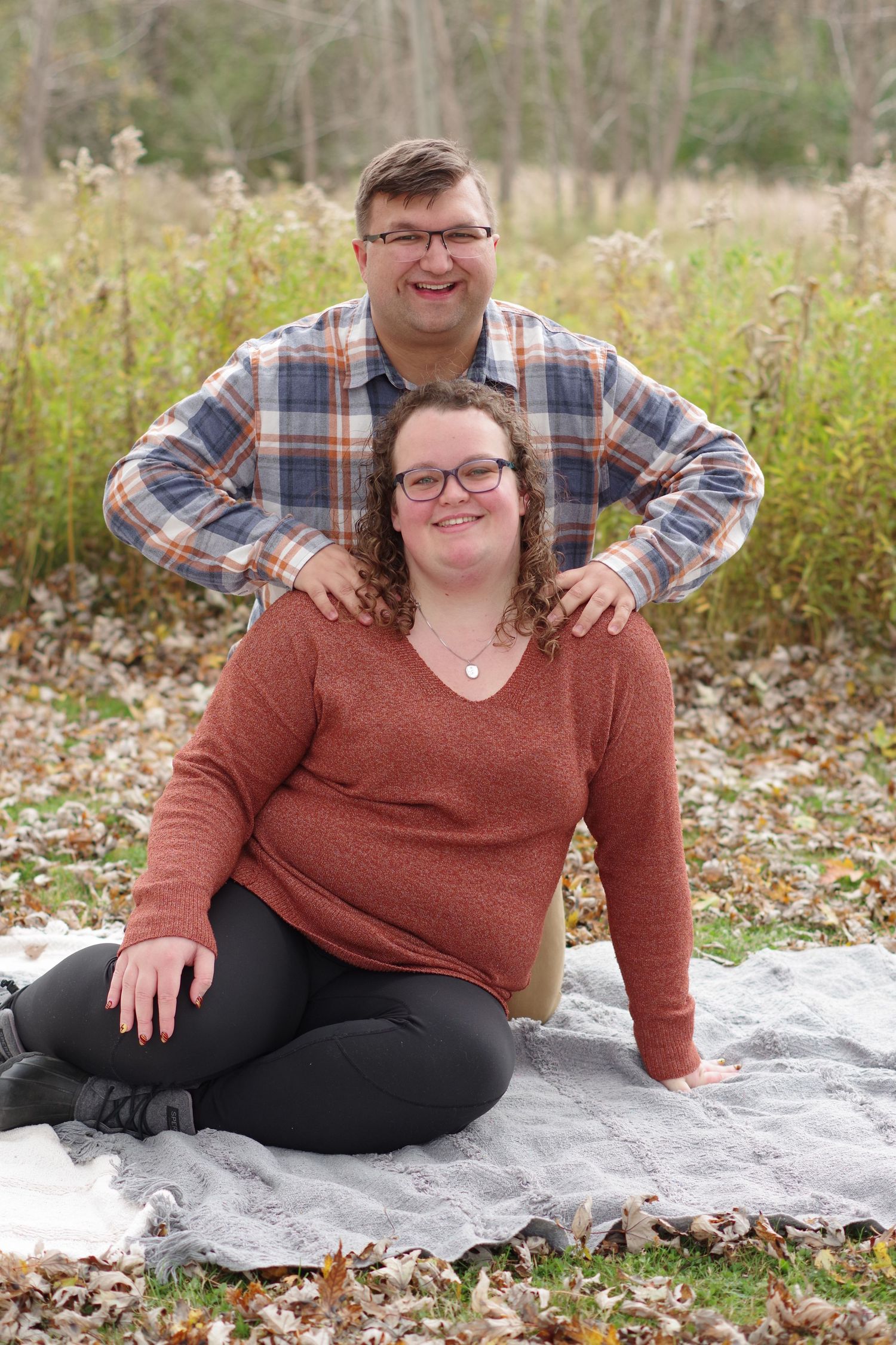 Couple posing on blanket surrounded by fall foliage and tall grass.