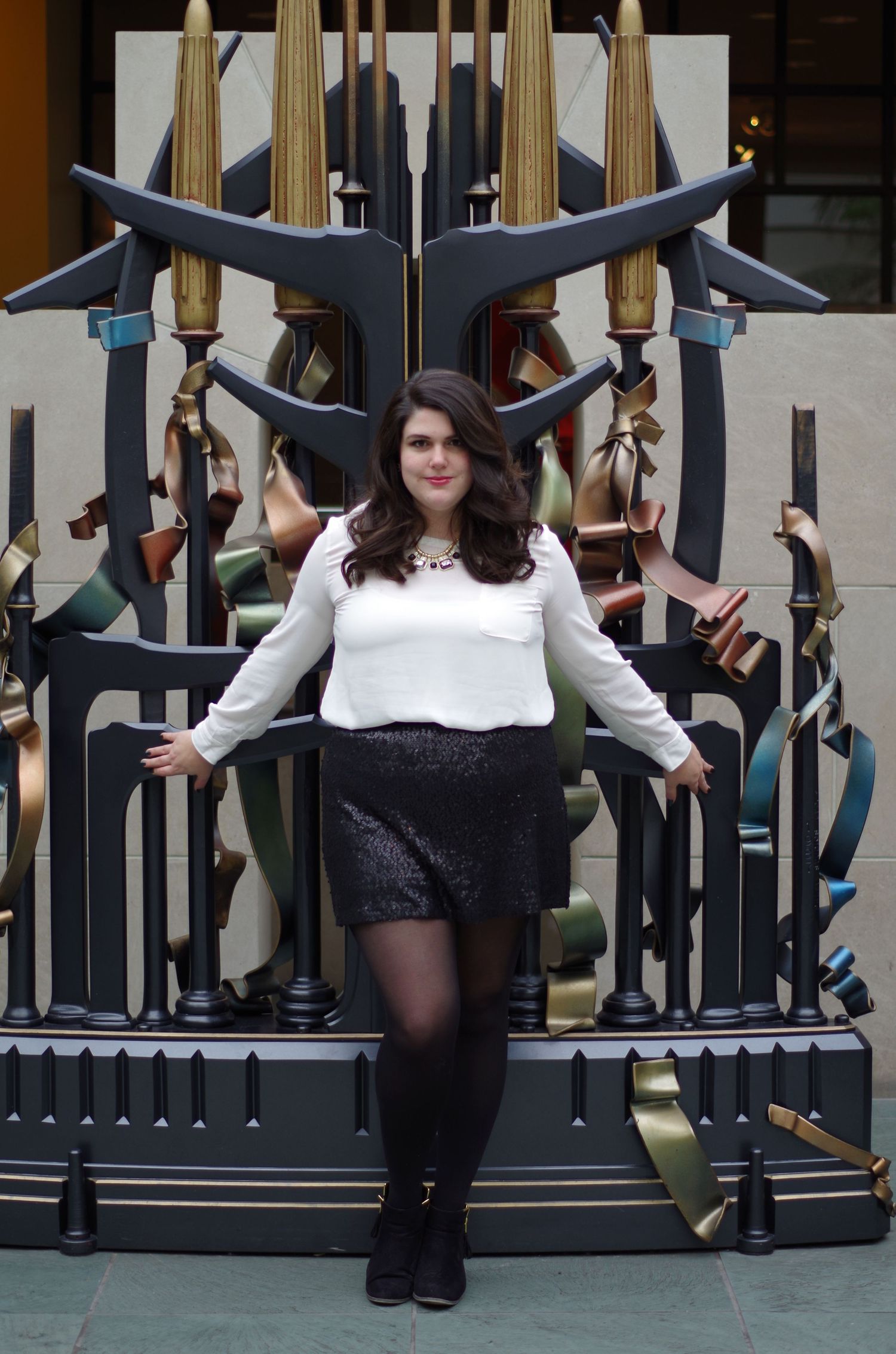A person in white top and sparkly skirt poses against decorative metal gates.