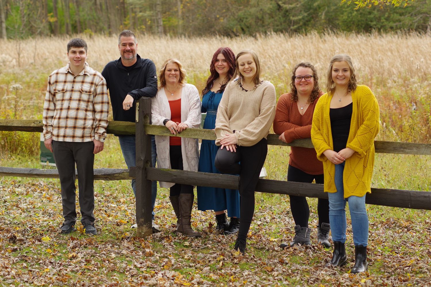 Group lined up along wooden fence with fall foliage and field in background.