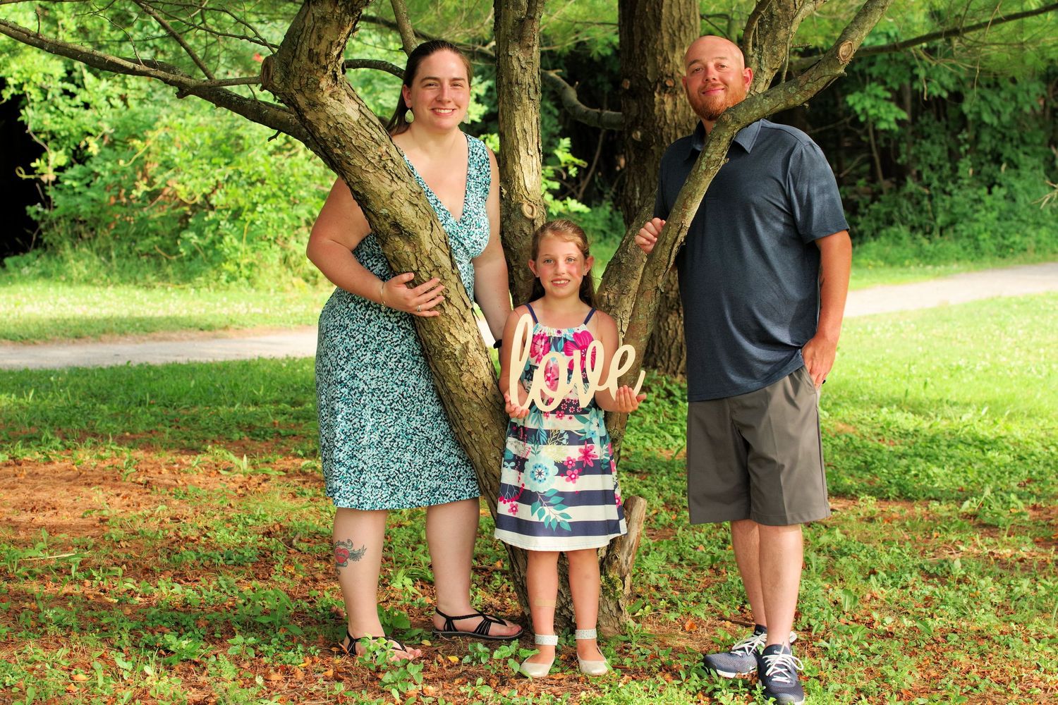 Family members stand between trees for a casual outdoor portrait in a sunny park.