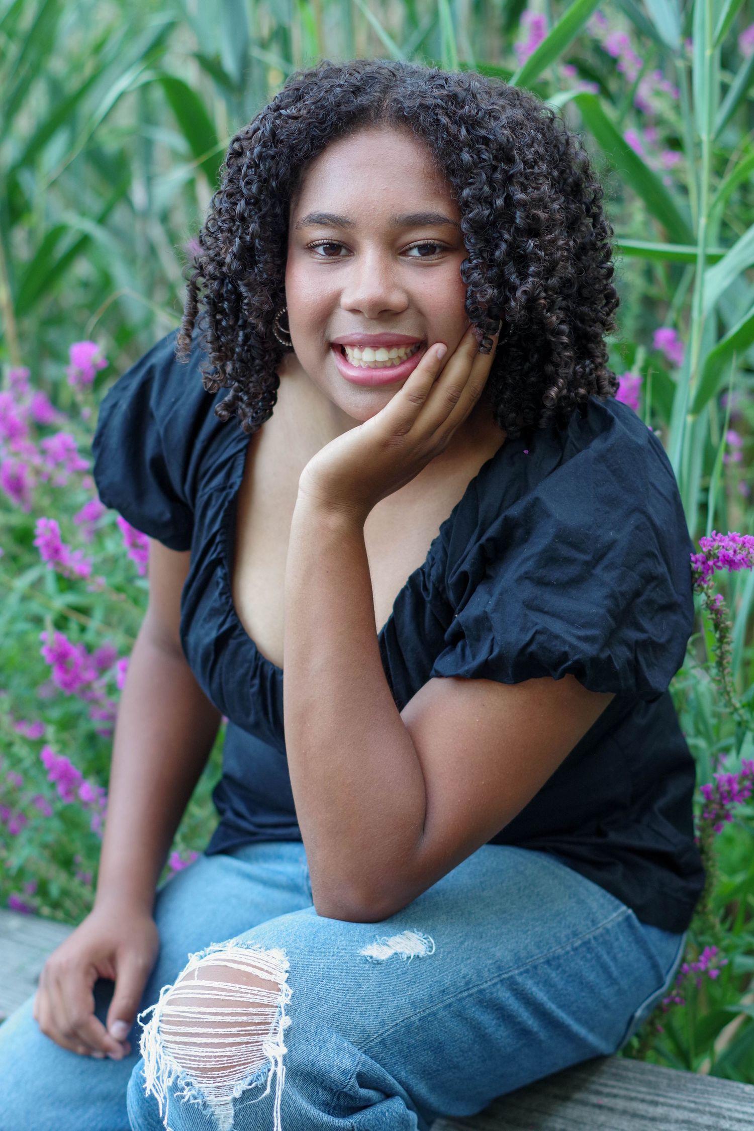 A joyful portrait session in a garden with distressed denim jeans against a backdrop of green plants and purple flowers.