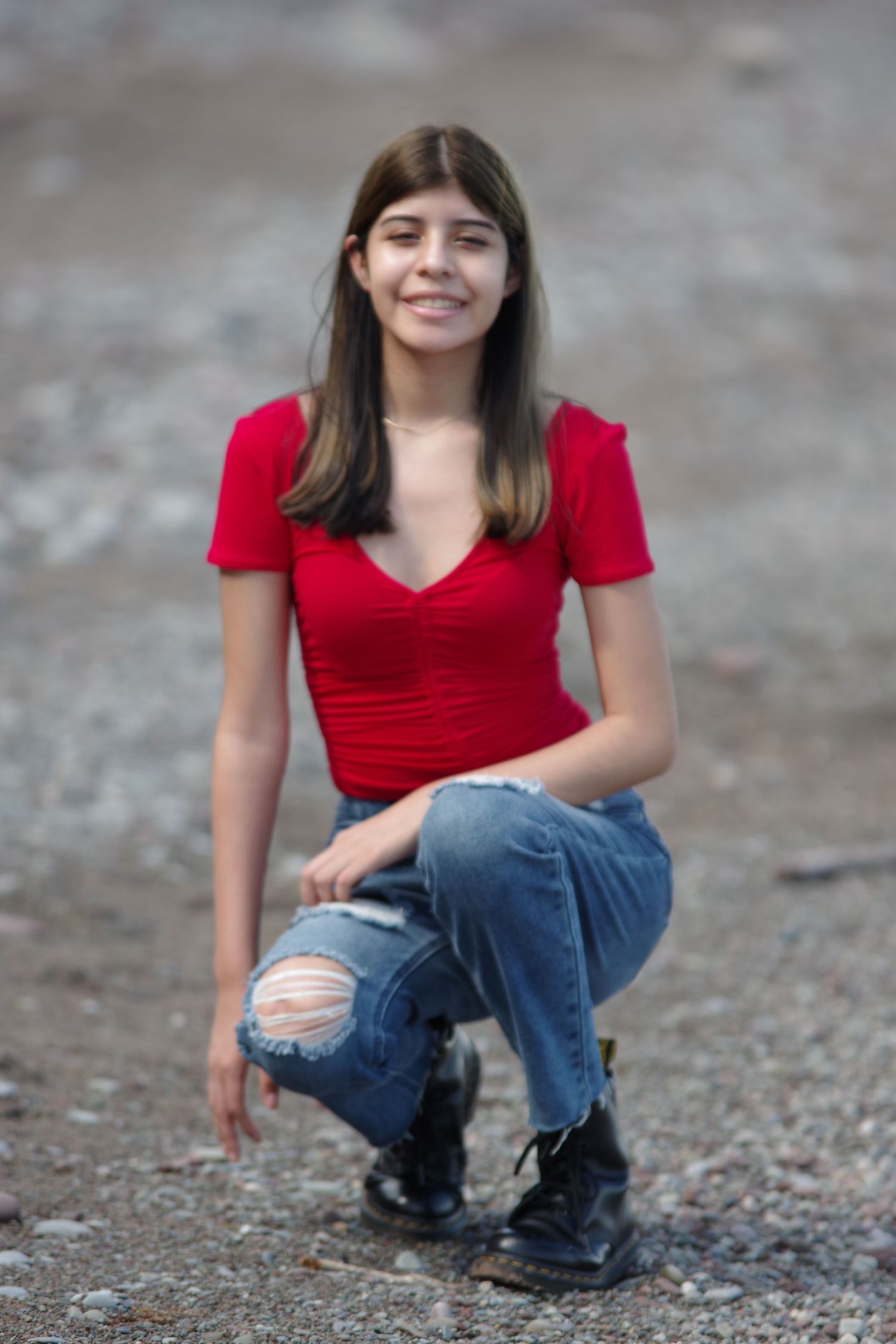 Portrait session on gravel ground showing casual poses in ripped jeans and red top.