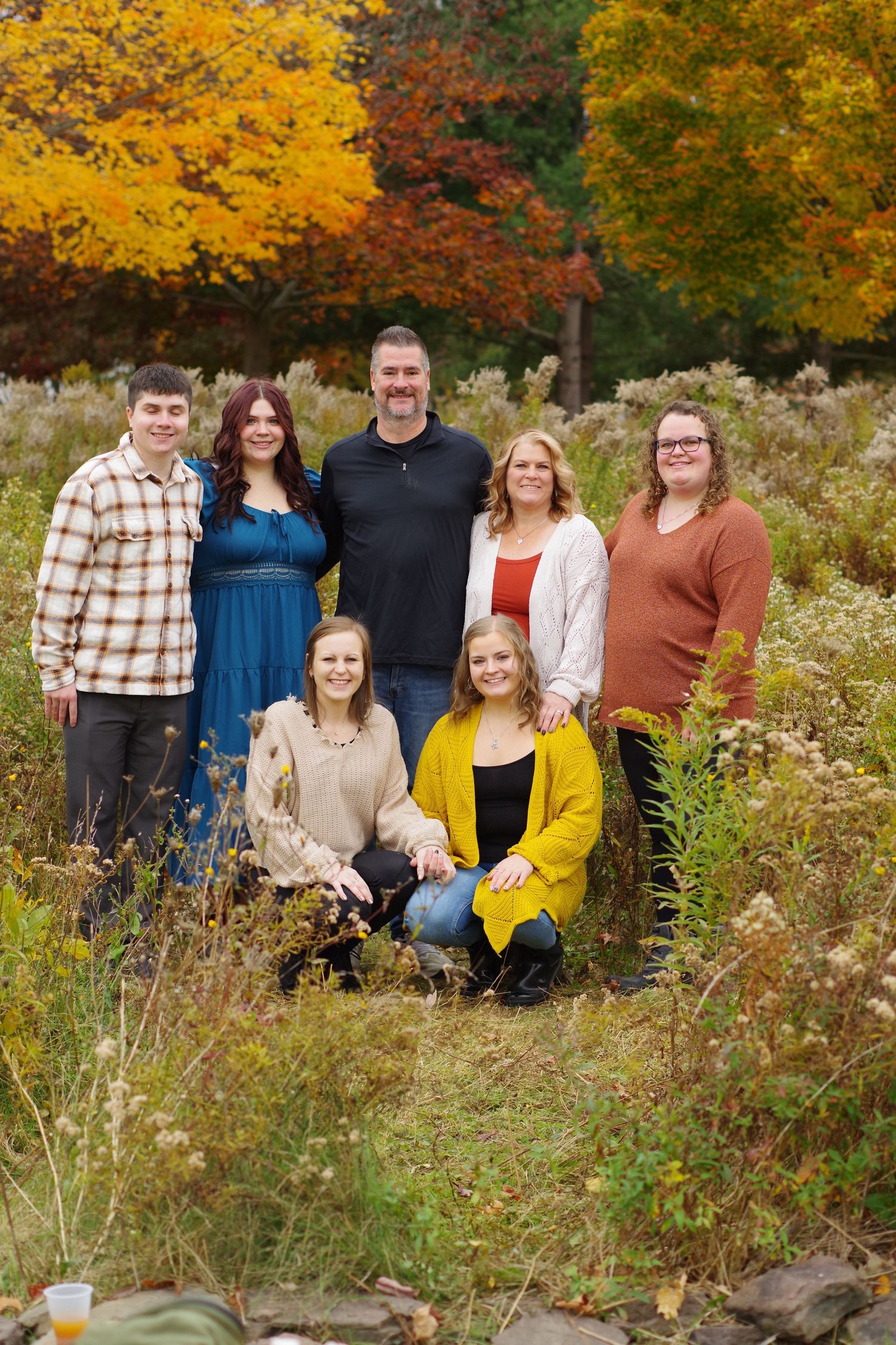 Group portrait of family members standing together in front of vibrant autumn trees.