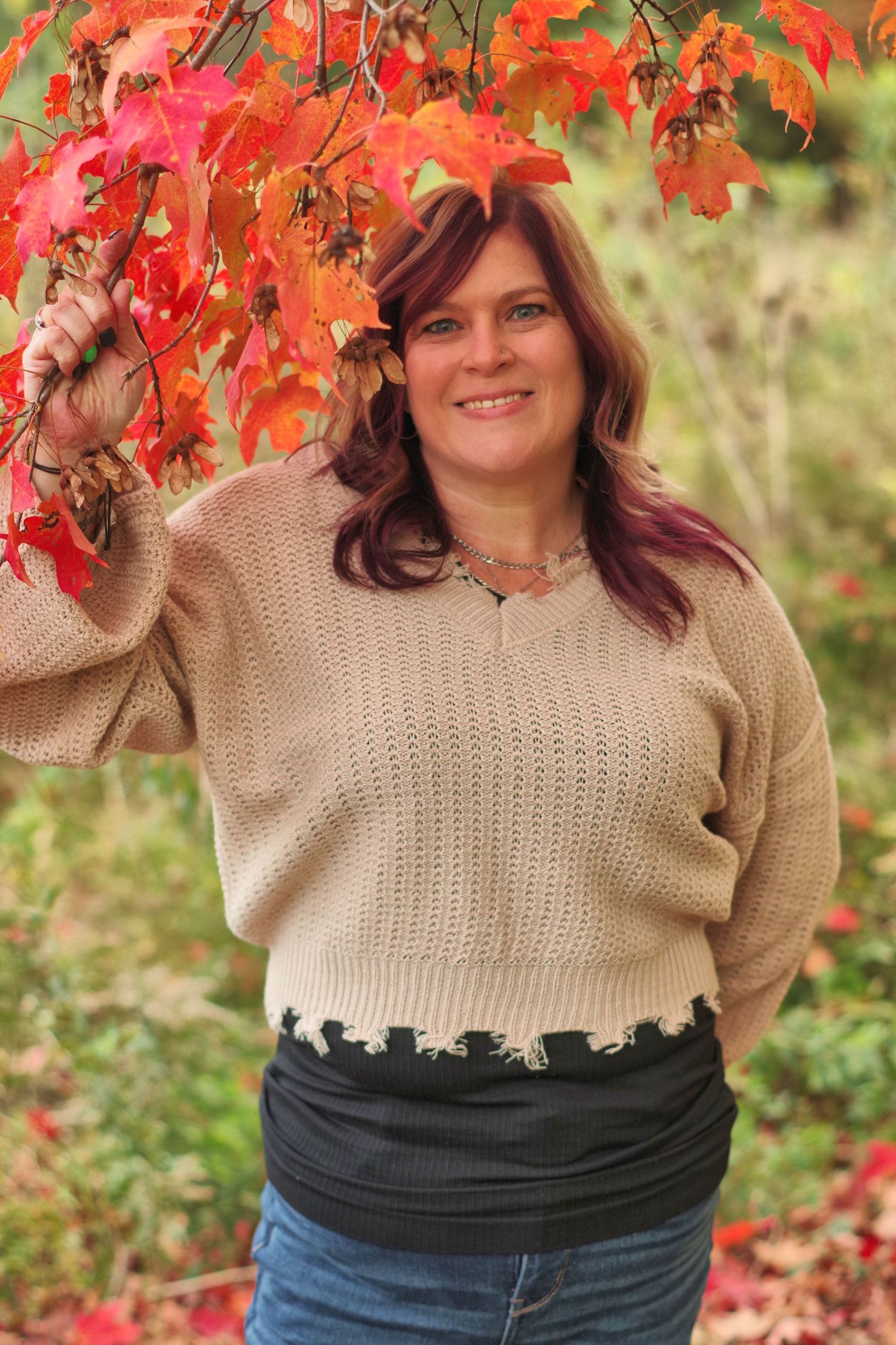 Autumn portrait under bright red maple leaves wearing beige sweater and jeans.