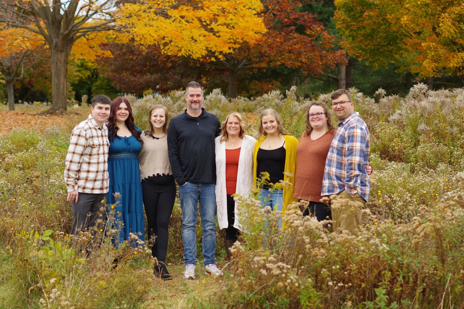Group photo of friends or family standing together against vibrant fall foliage background.