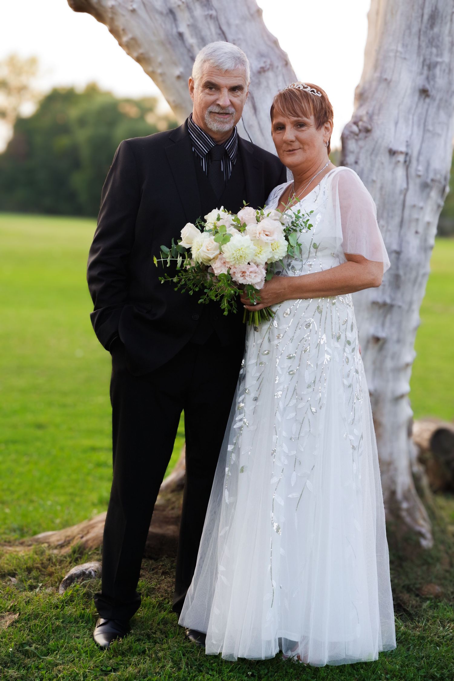 Couple poses together at wedding with bride holding white floral bouquet.
