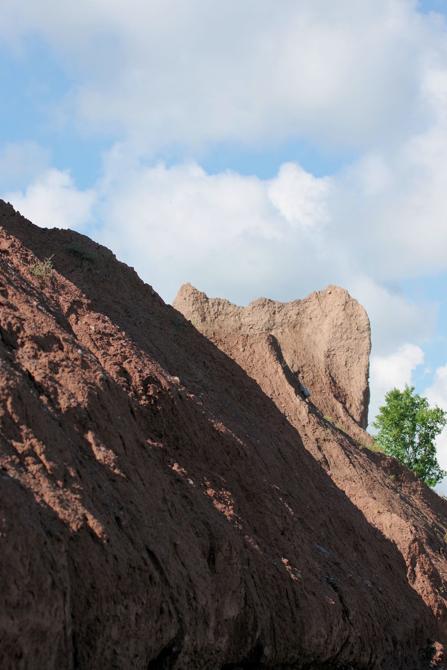 Rocky cliffside formation with steep slopes against a cloudy blue sky.