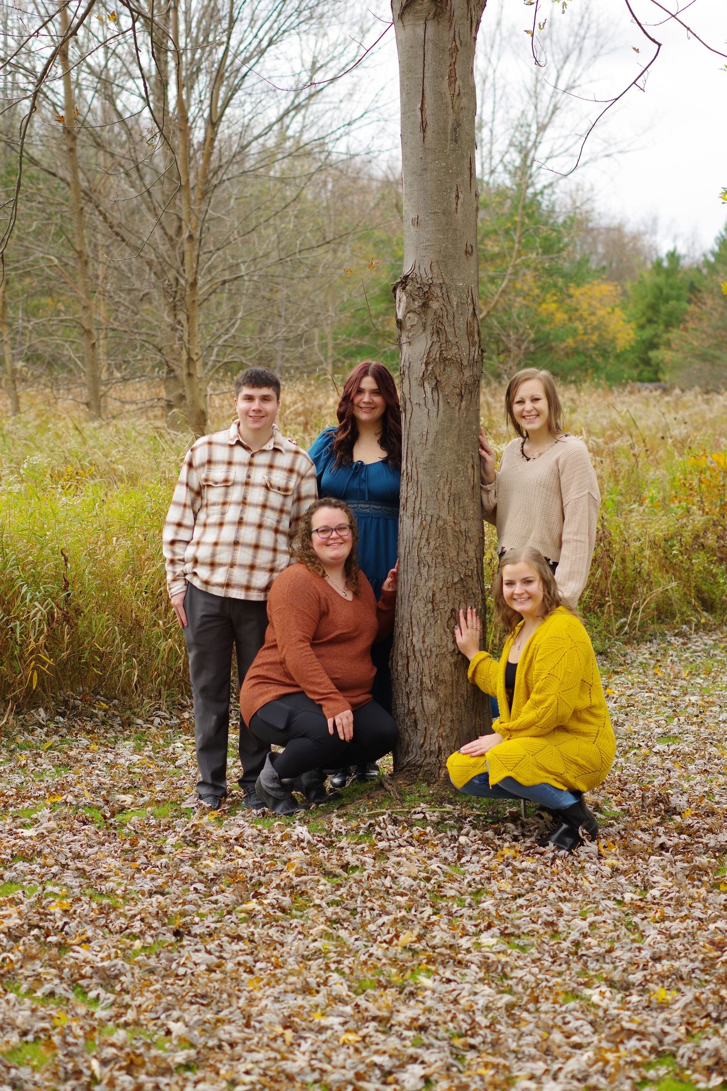 Family group poses together by a tree trunk in a fall woodland setting.