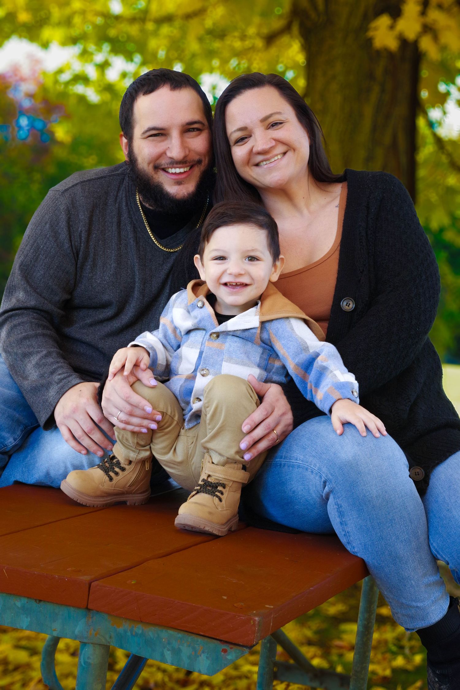Fall family portrait on red bench with autumn foliage in background.