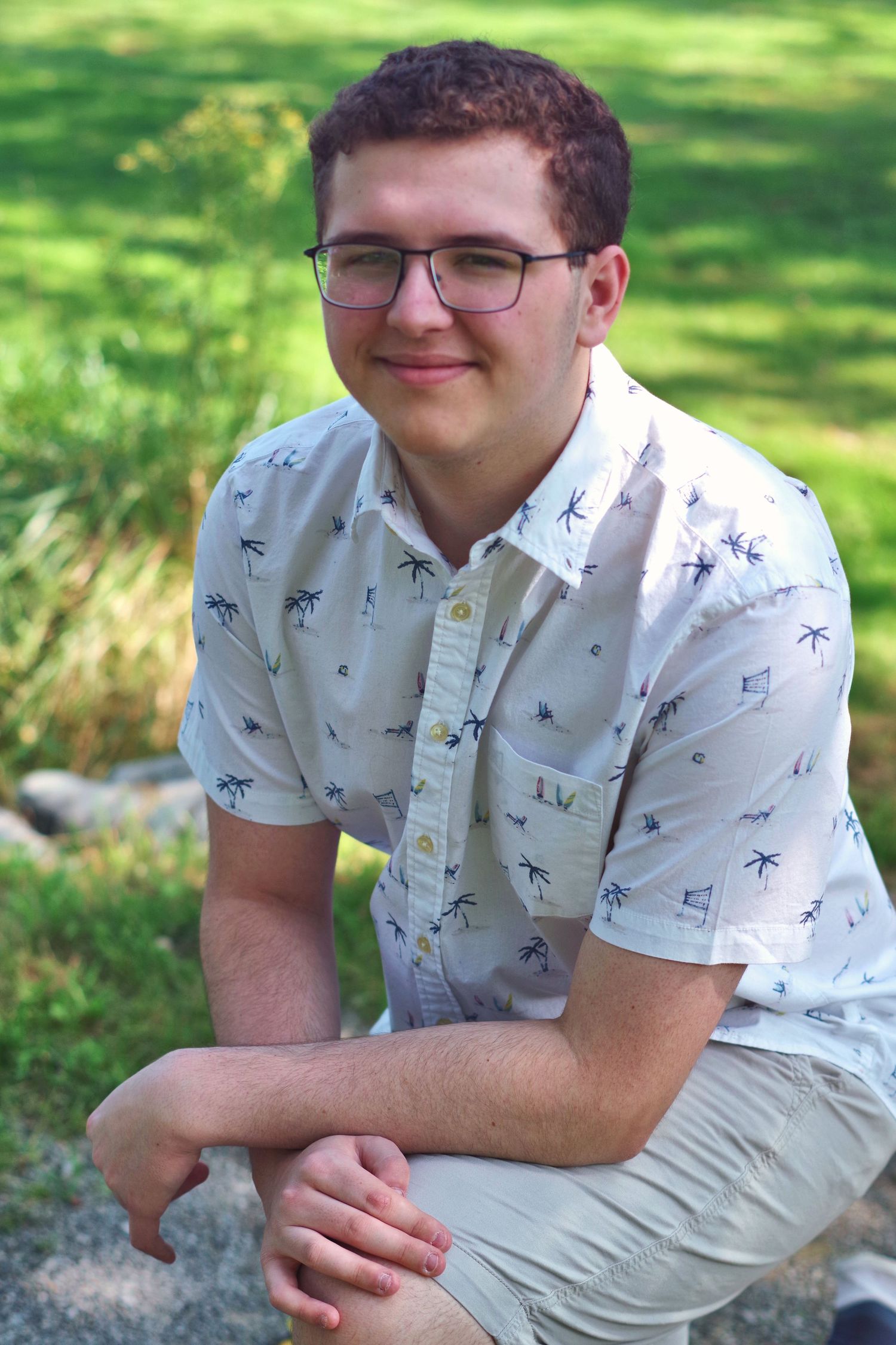 Outdoor portrait series in palm tree patterned shirt against natural green background.