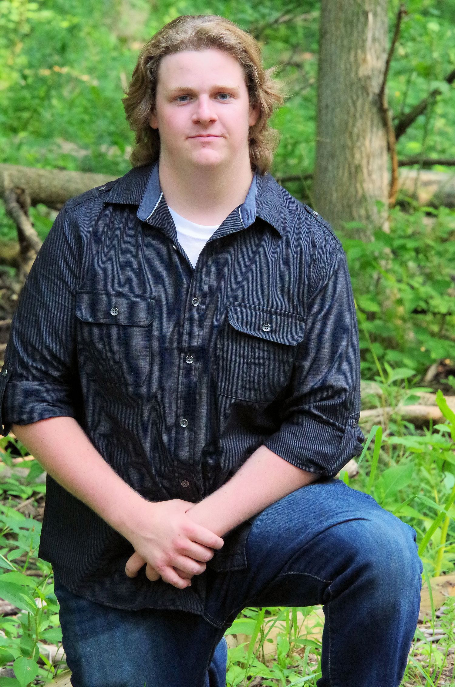 Person in casual attire sitting against a forest backdrop.
