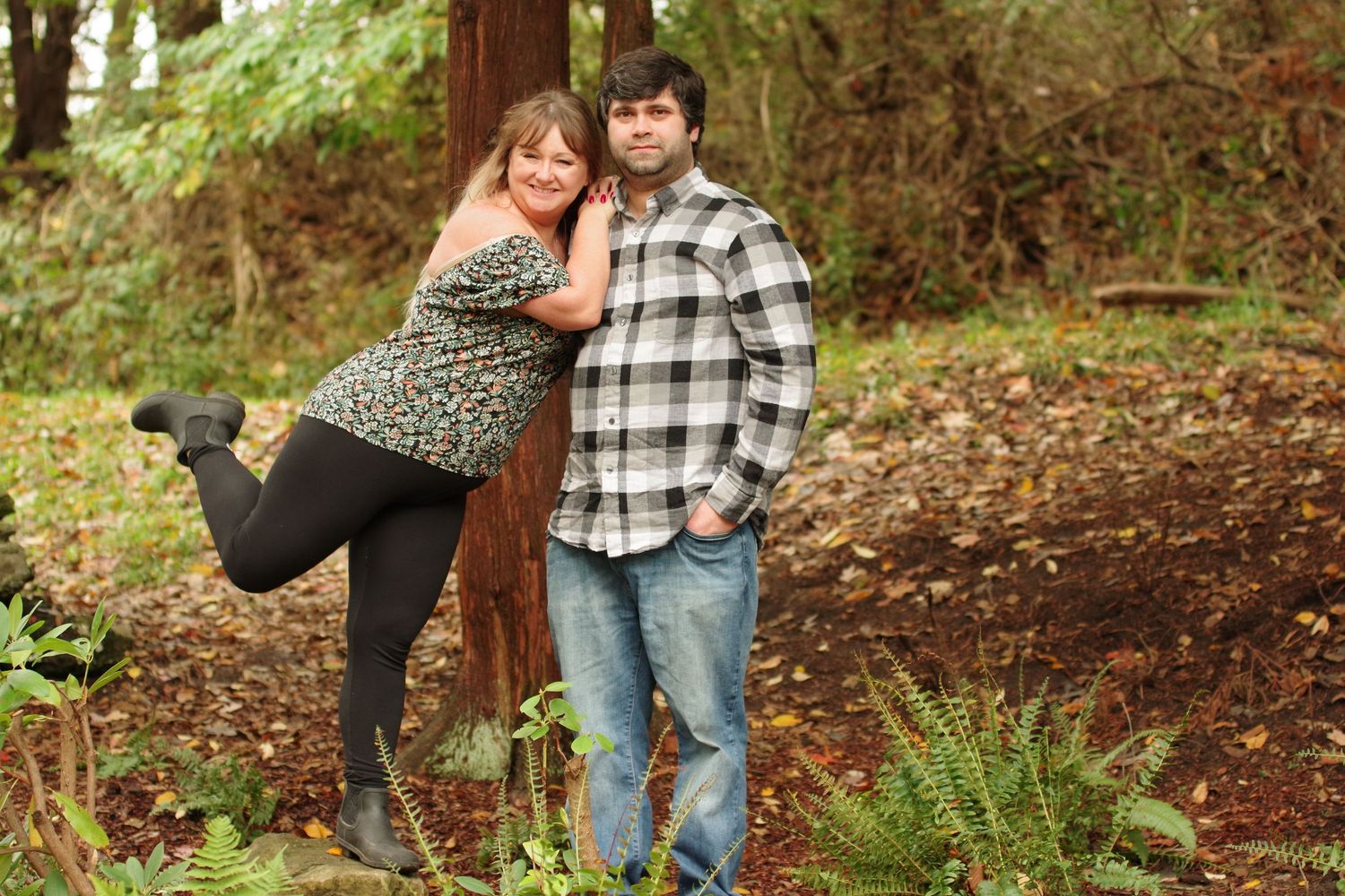 Couple embracing near stone wall in wooded outdoor setting.