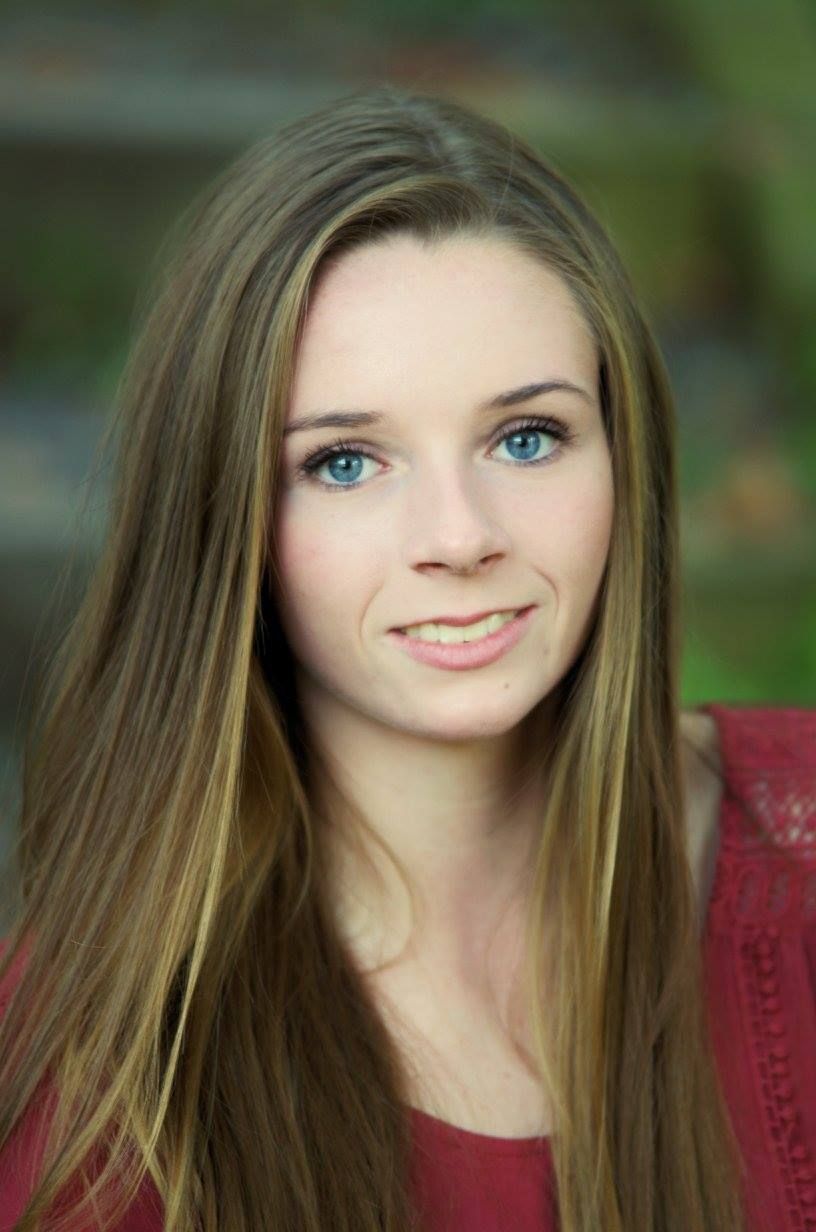 Portrait against blurred green background showcasing long straight hair and red top.