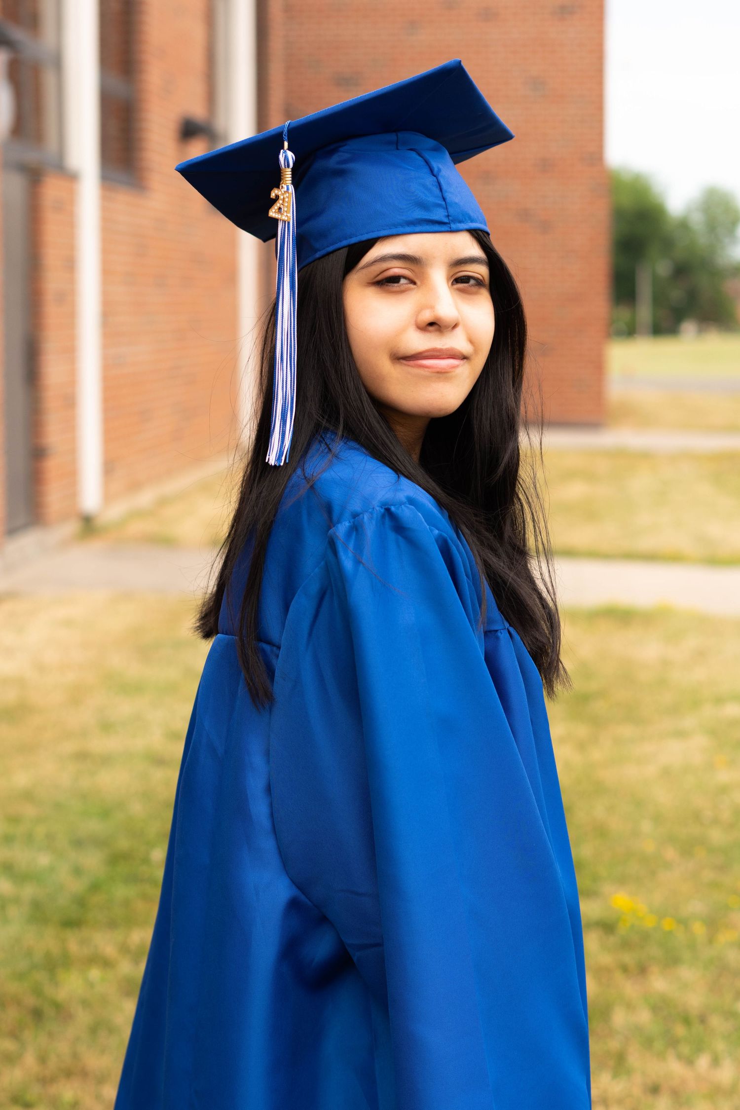Graduate in blue cap and gown poses outdoors against brick building.