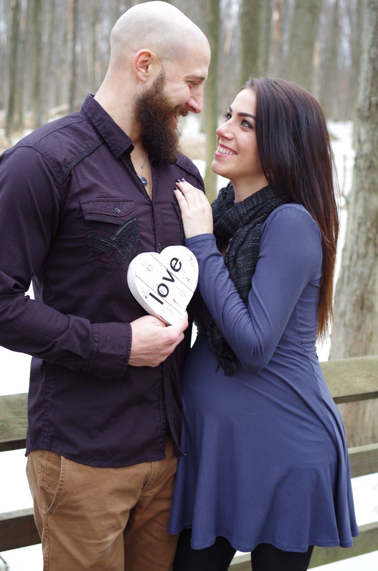 Winter engagement photo session shows couple holding love signs in snowy woods.