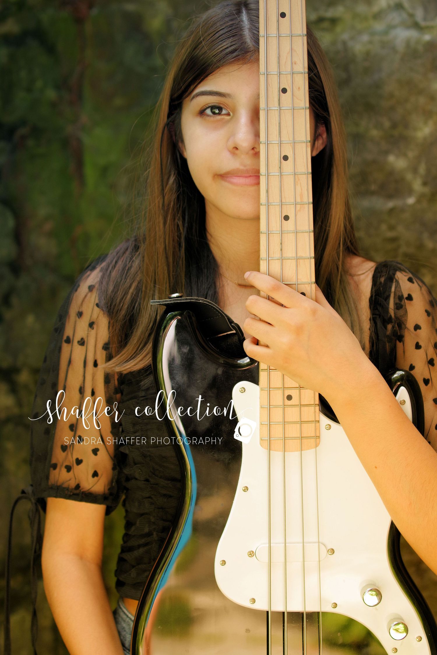 Close-up portrait with bass guitar wearing black lace top against natural background.