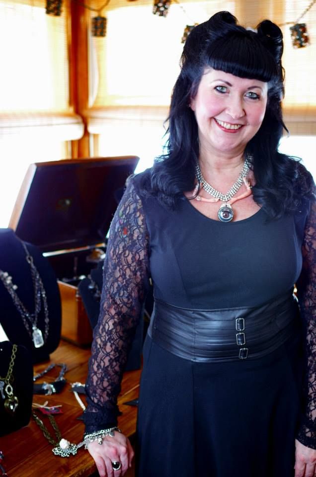 Woman in black lace dress posing in elegant indoor setting with natural lighting.