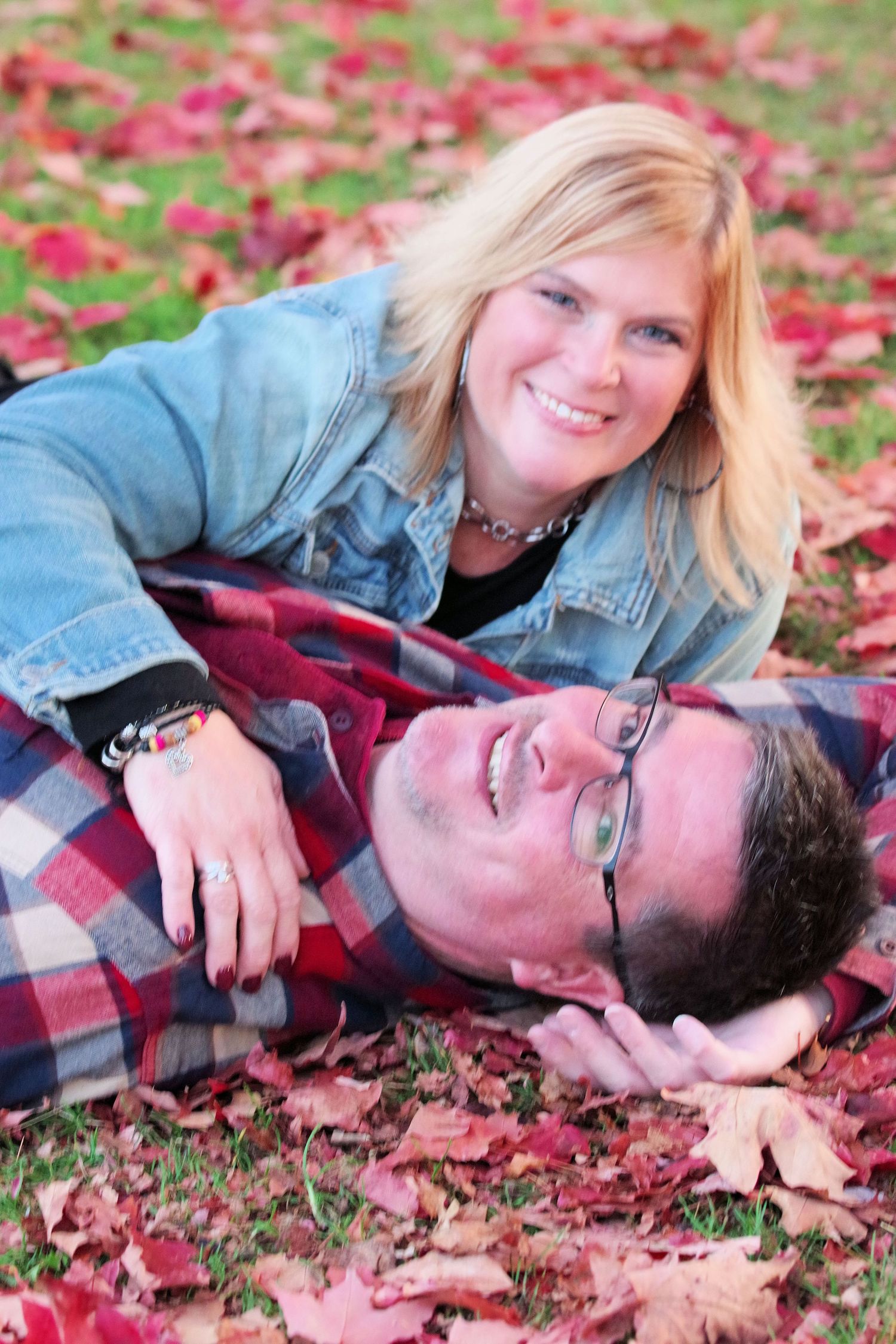 Couple lying together on red autumn leaves in a romantic outdoor photoshoot.