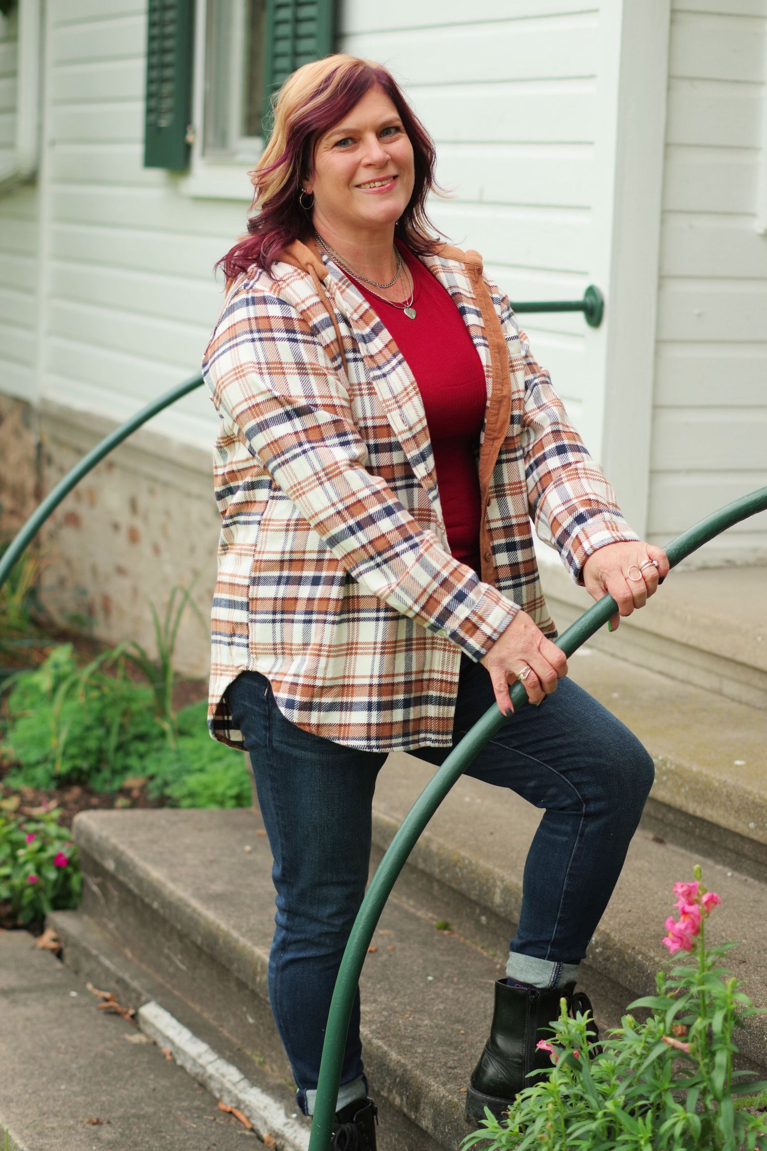 Person in plaid flannel and jeans poses on steps while holding a green handrail.
