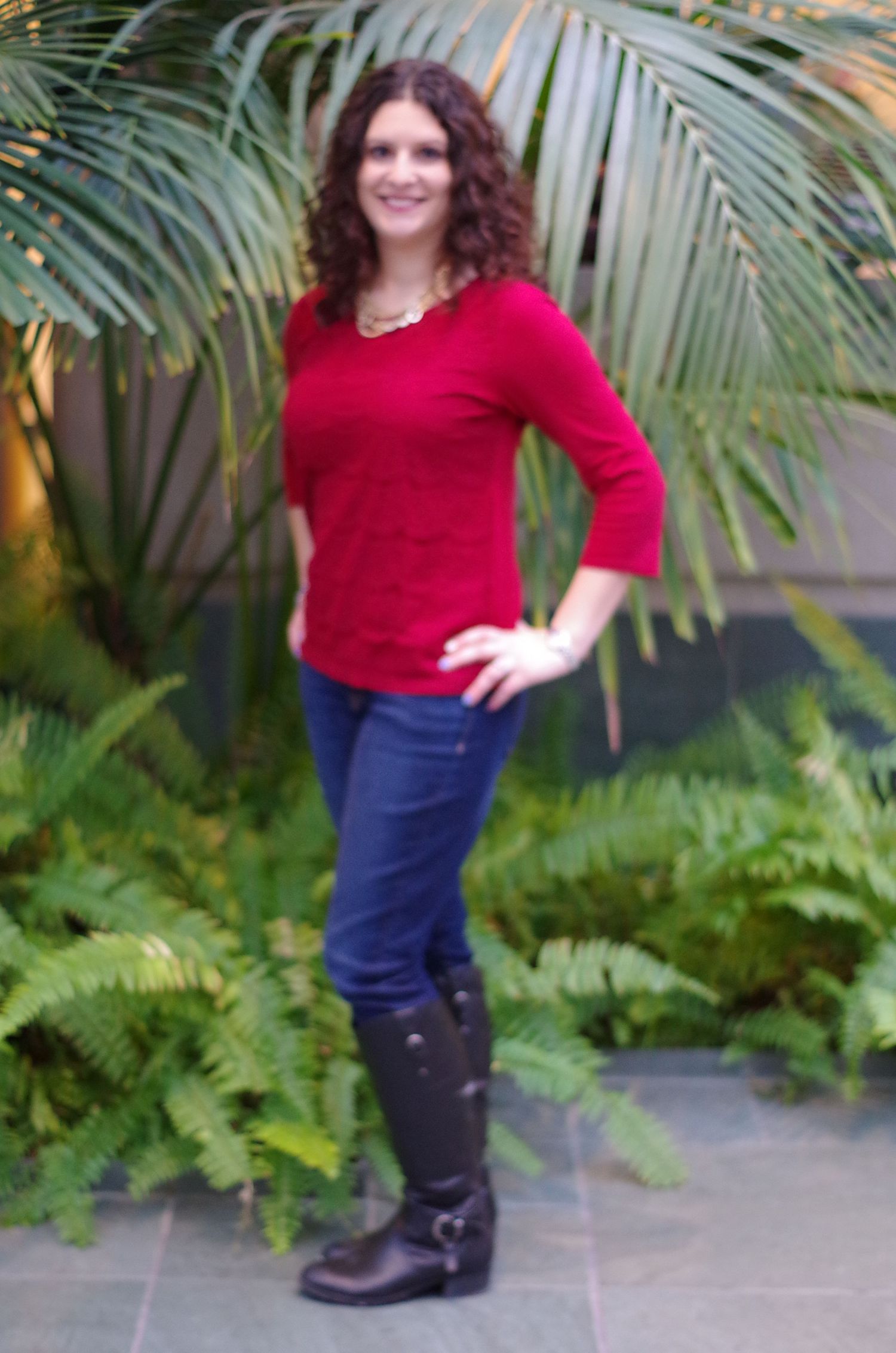A person in a red sweater poses against tropical foliage background.