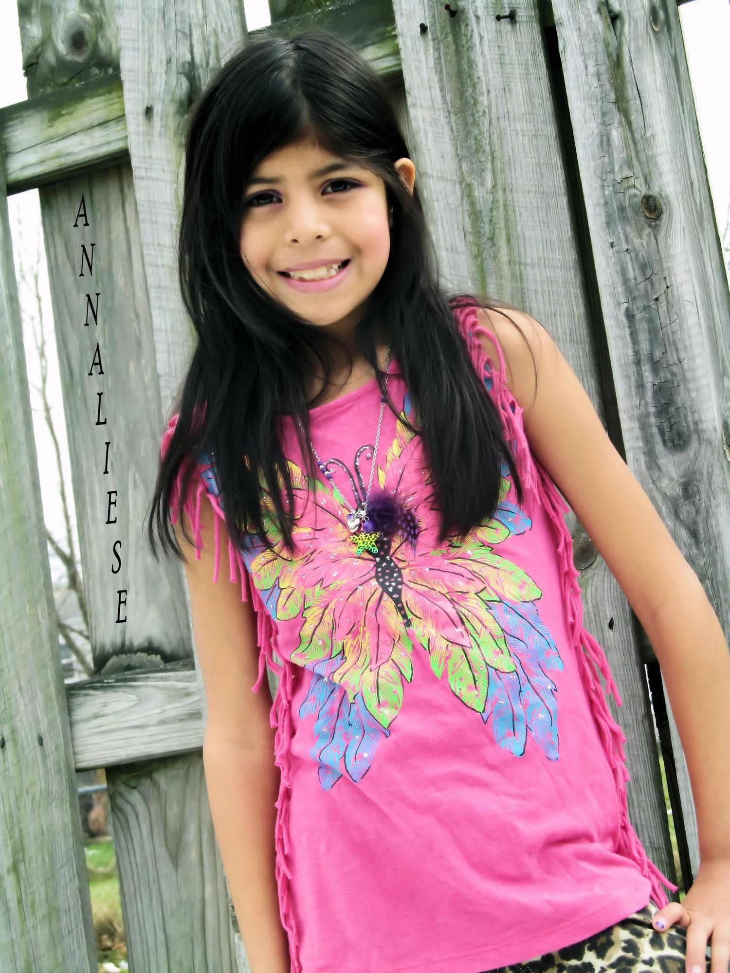 A person wearing a bright pink floral tank top poses against a weathered wooden fence.