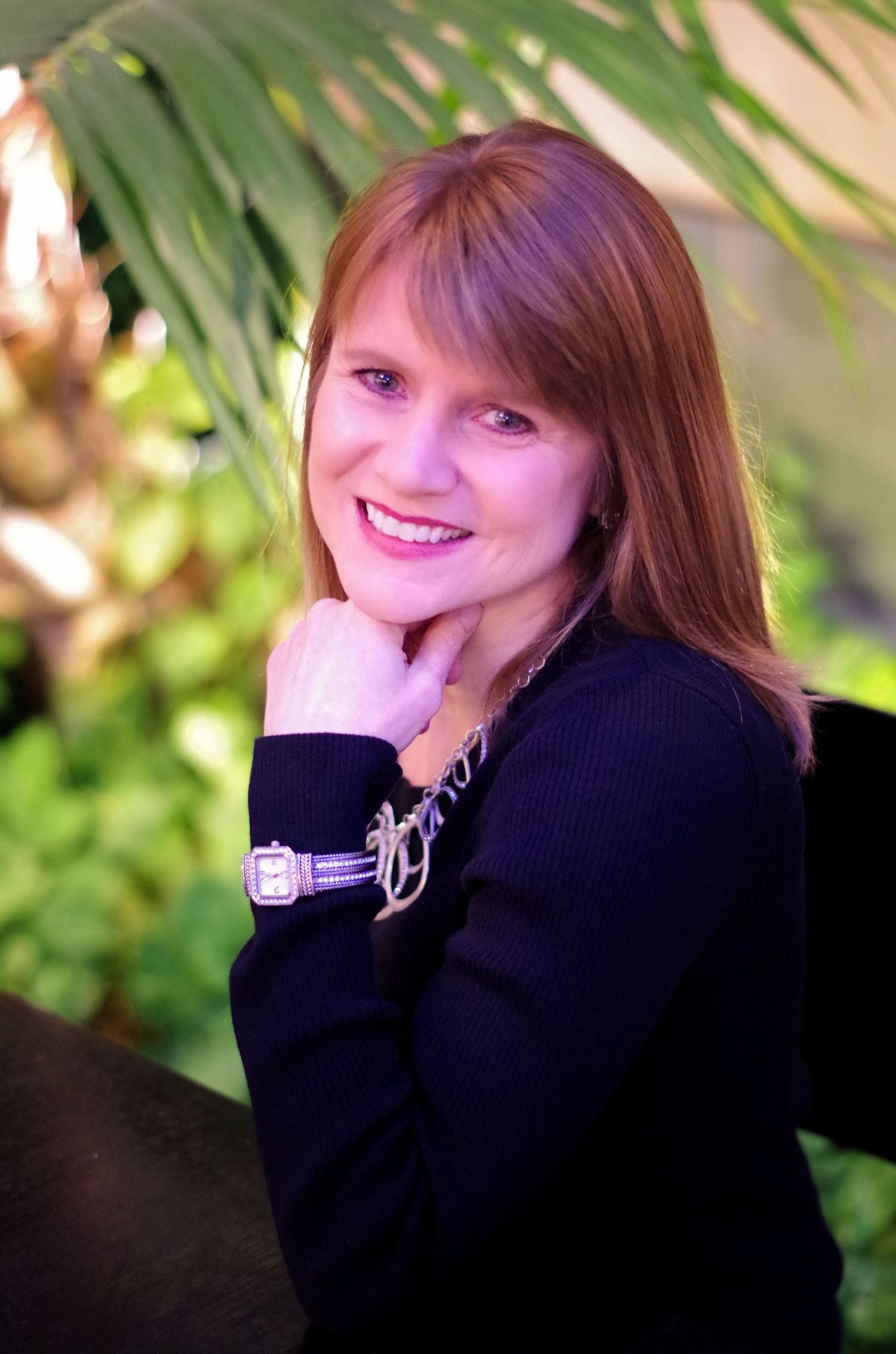 Professional portrait of someone in black attire against a tropical plant background.
