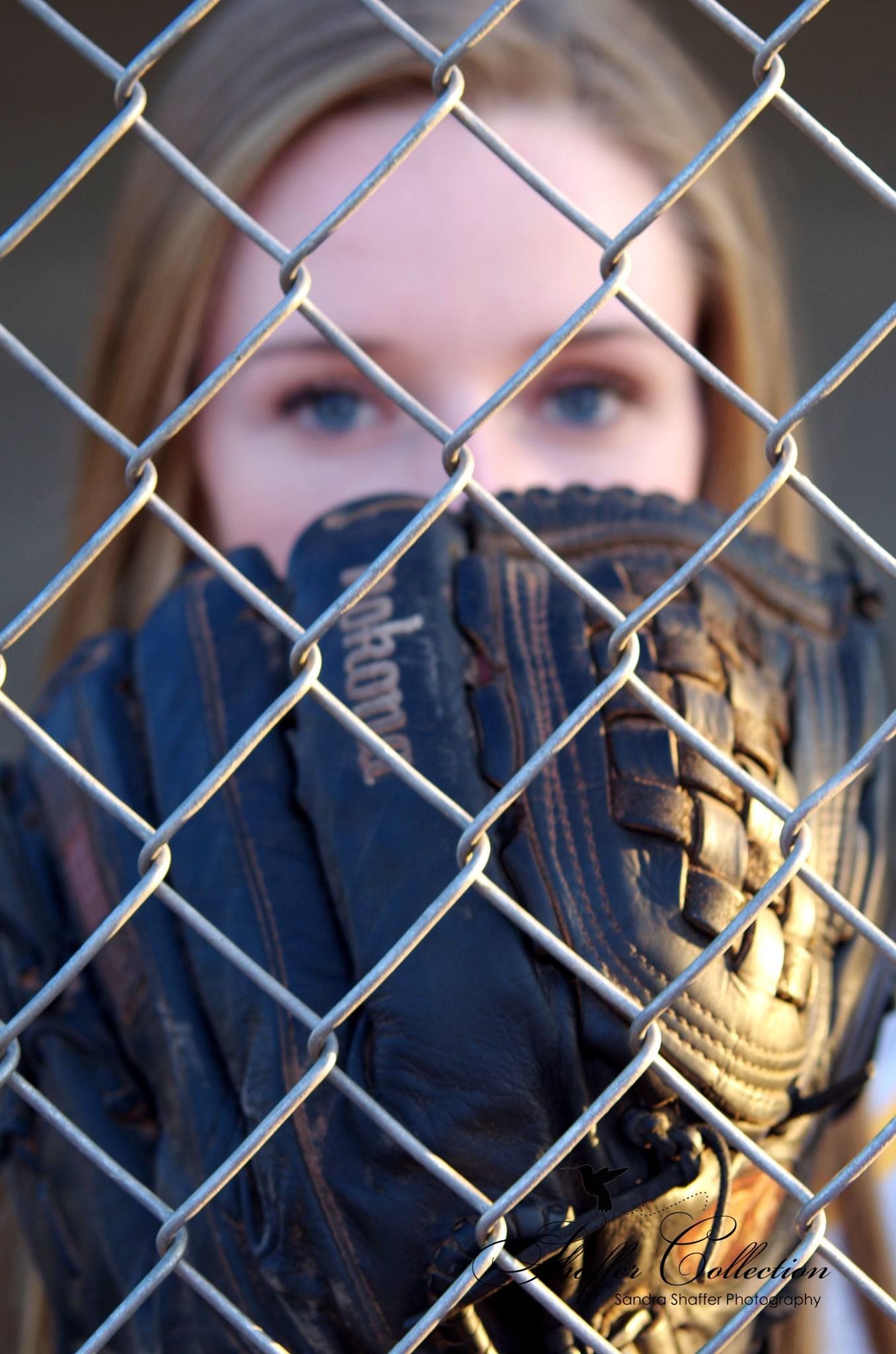 Baseball player seen through chain link fence wearing protective gear.