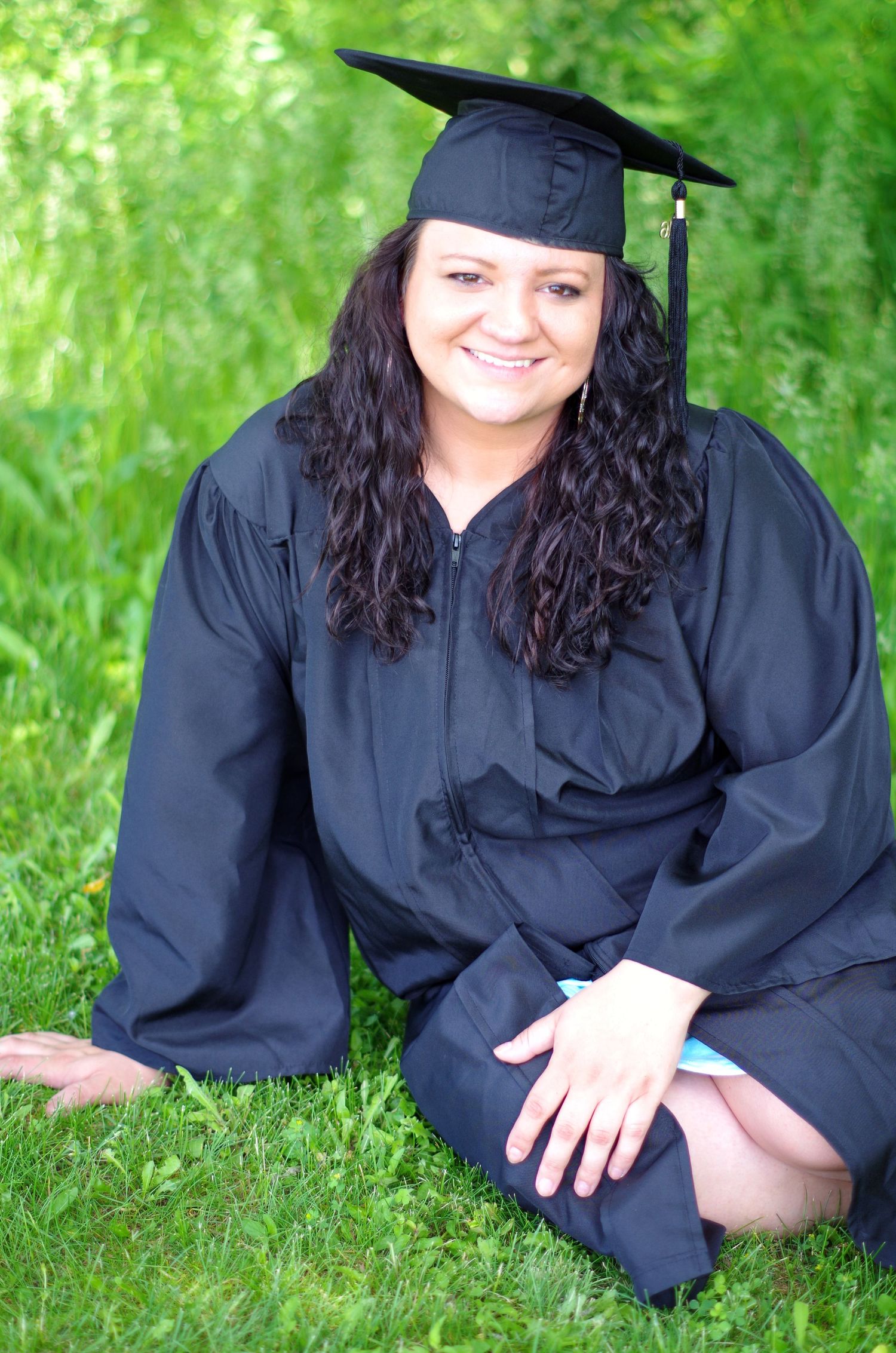 Graduate in black gown poses on grass during outdoor photo session.
