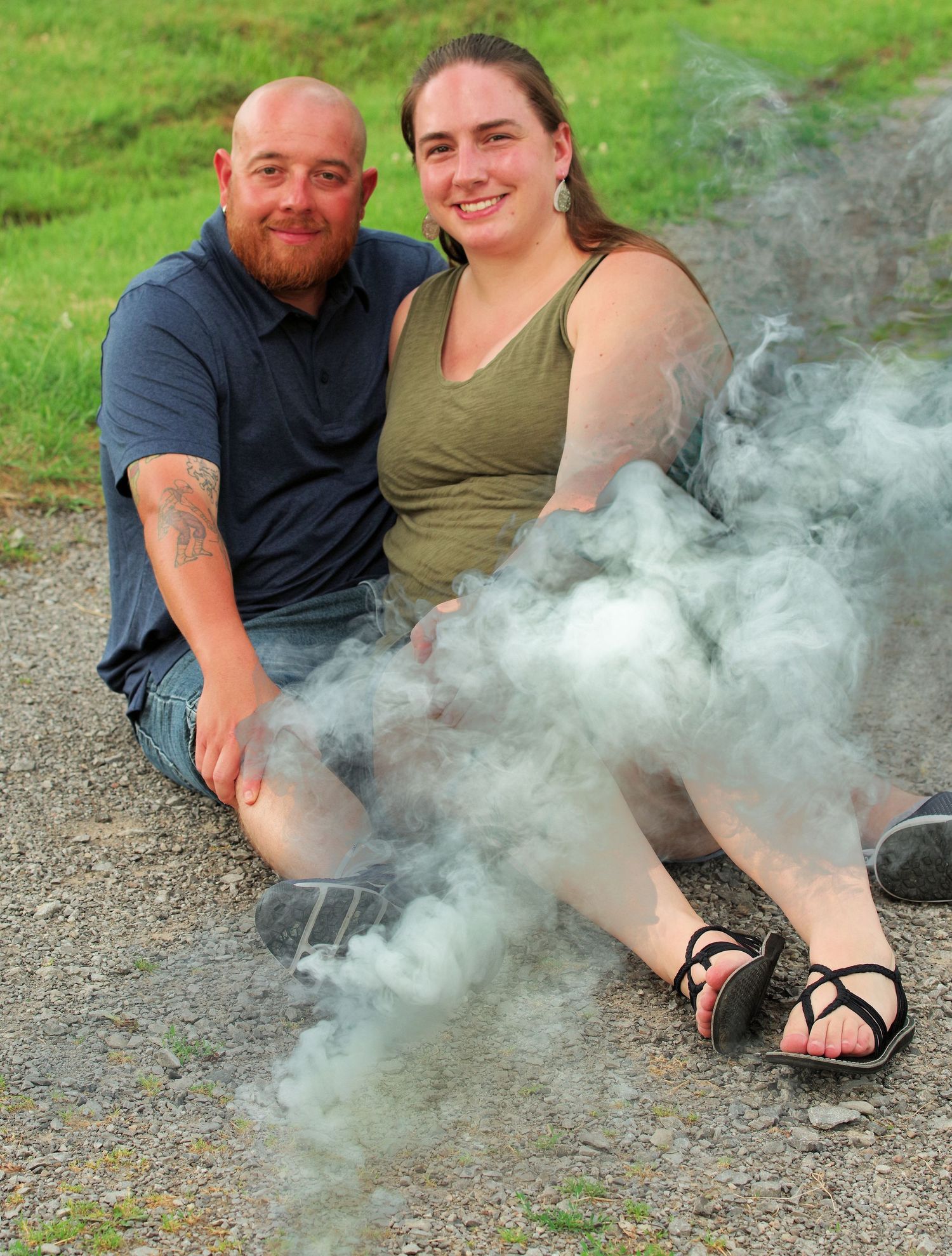 Couple sitting casually on ground with smoke effects in outdoor setting.