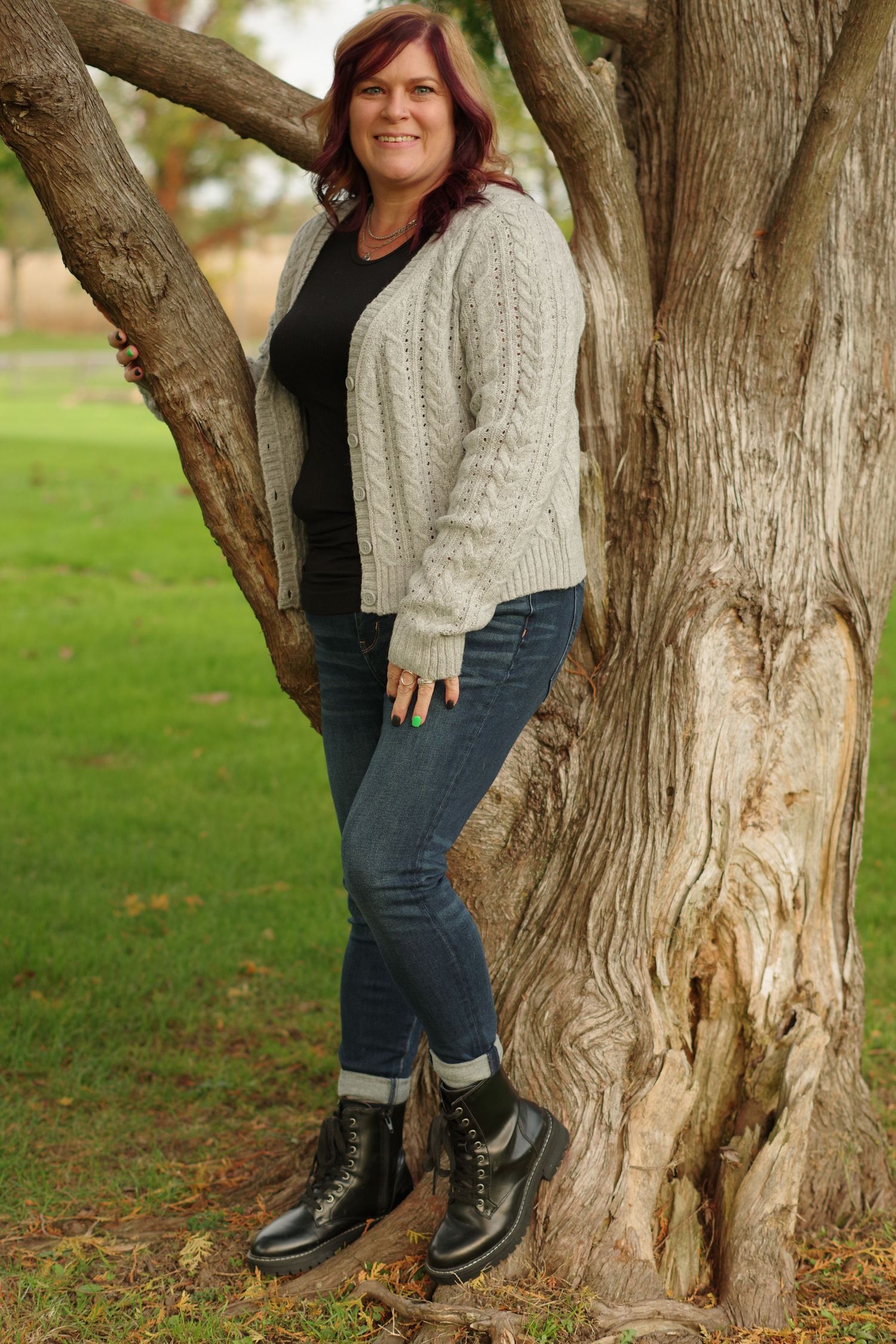Casual outdoor portrait leaning against large tree trunk wearing cable knit sweater and boots.