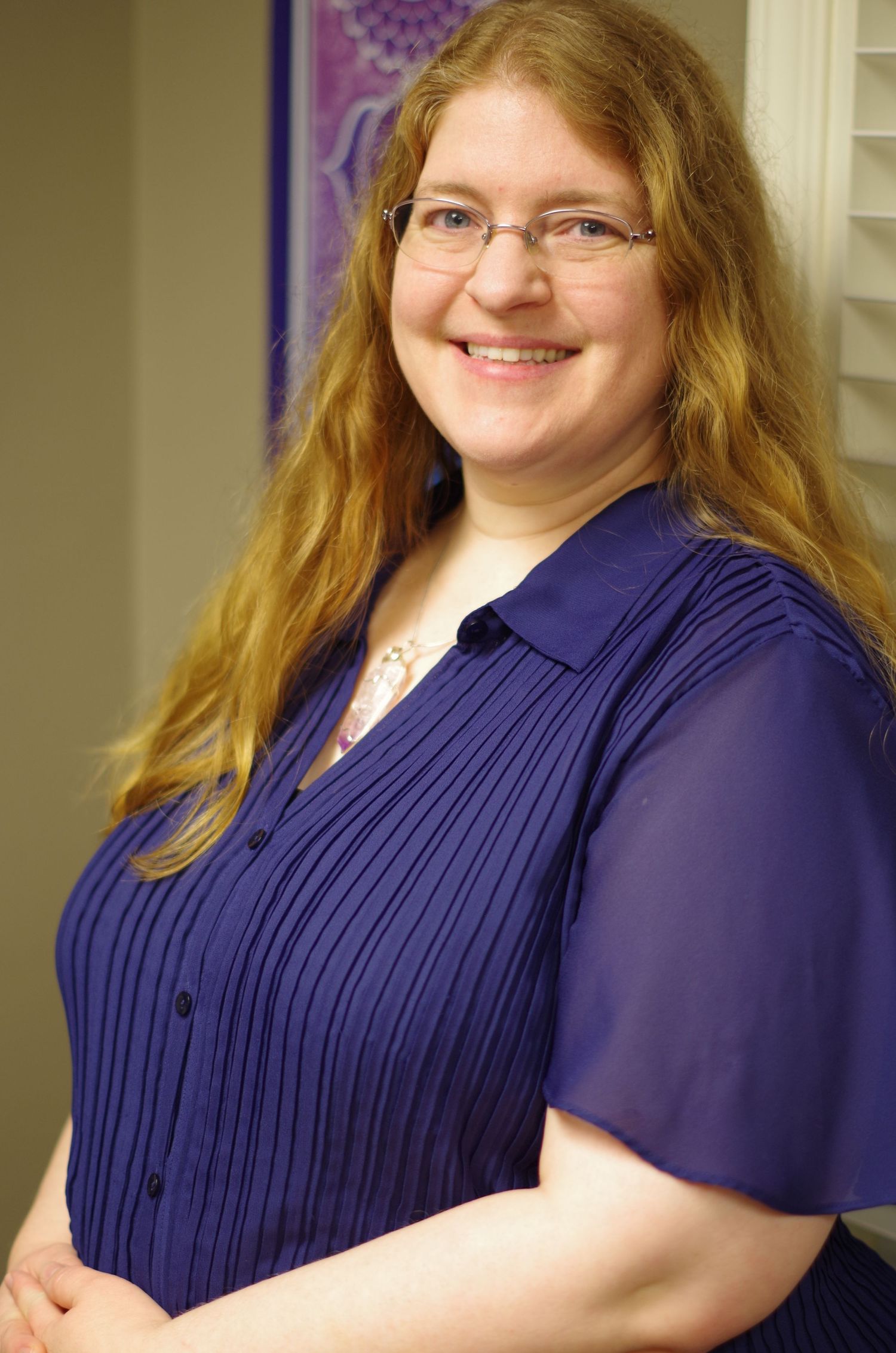 Side profile portrait of a person in a navy pleated blouse with wavy hair and glasses.