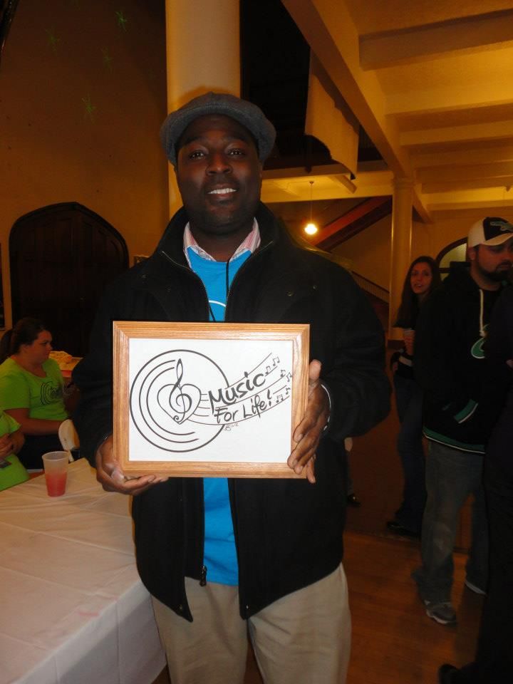 Several people displaying identical framed art pieces with musical symbols at an indoor event.