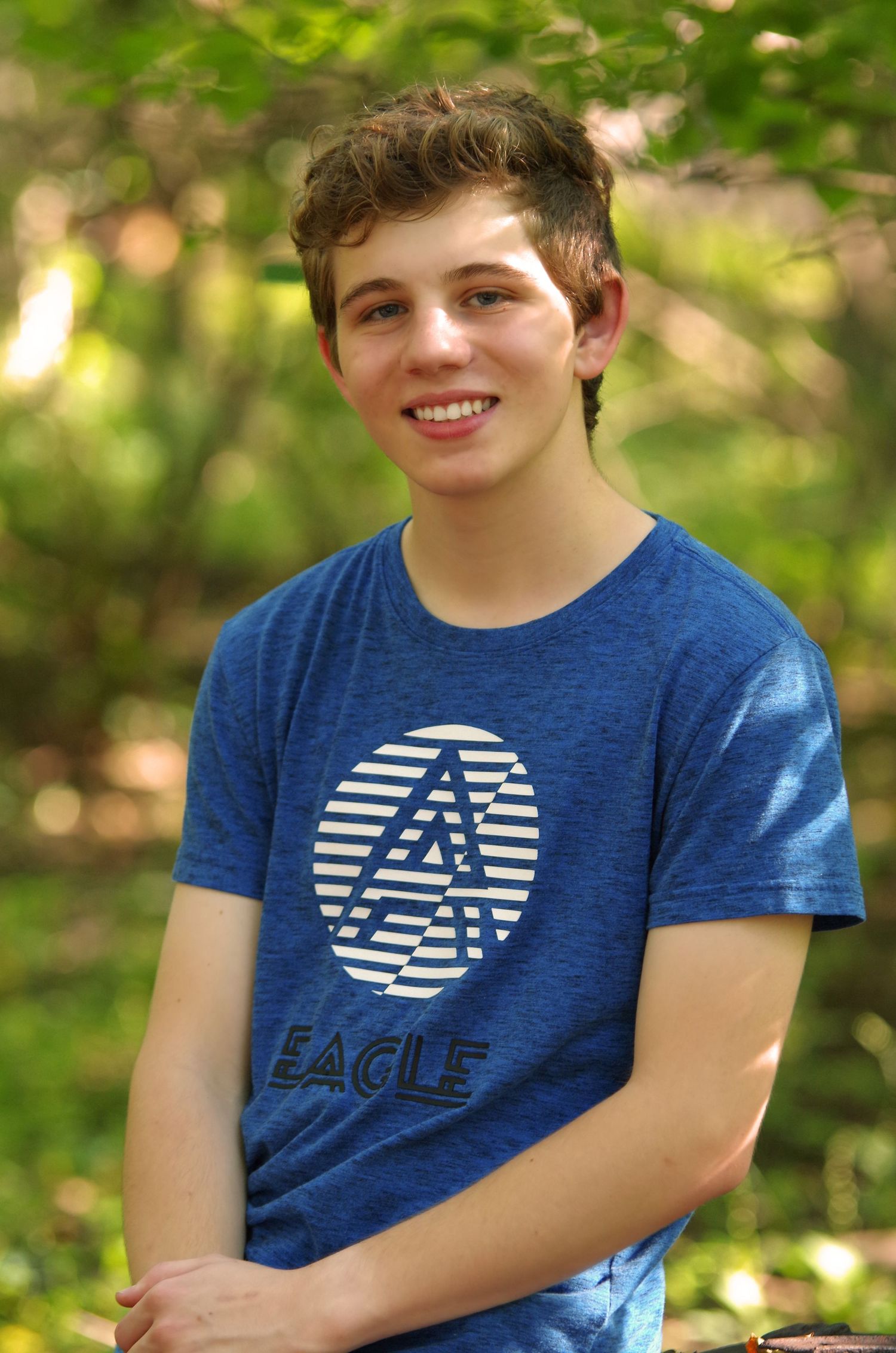 Person wearing a navy blue eagle logo t-shirt poses outdoors with green foliage in background.