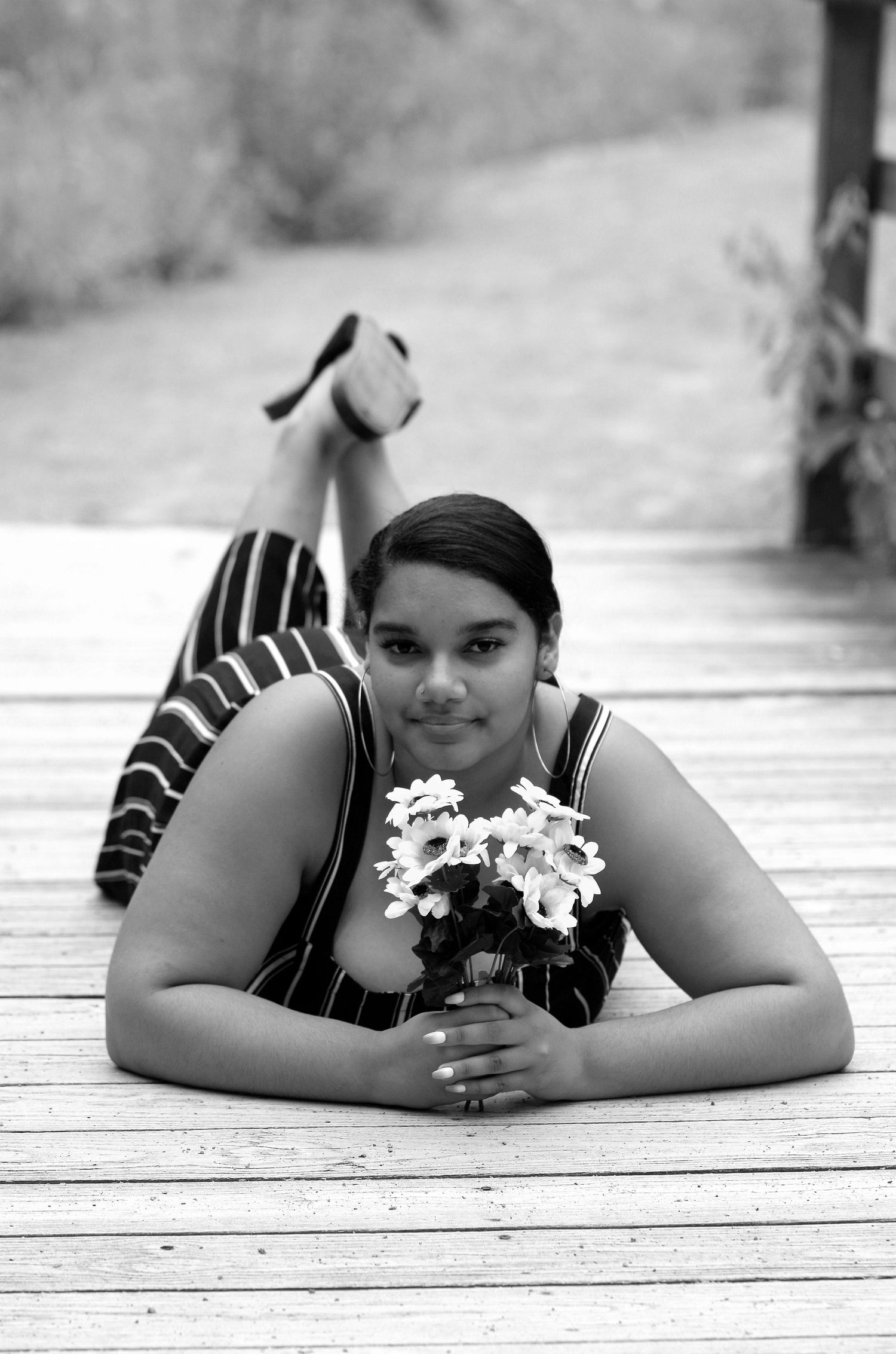A black and white portrait of someone lying on wooden decking holding white daisies.